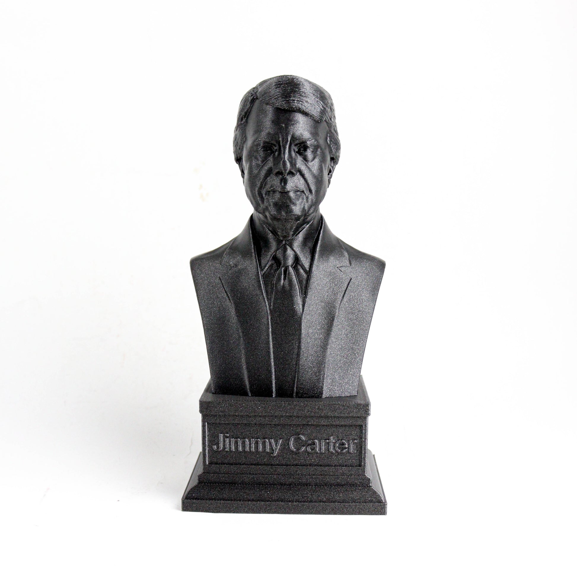 A black bust statue of a man wearing a suit and tie, with the name "Jimmy Carter" engraved on a pedestal below it.