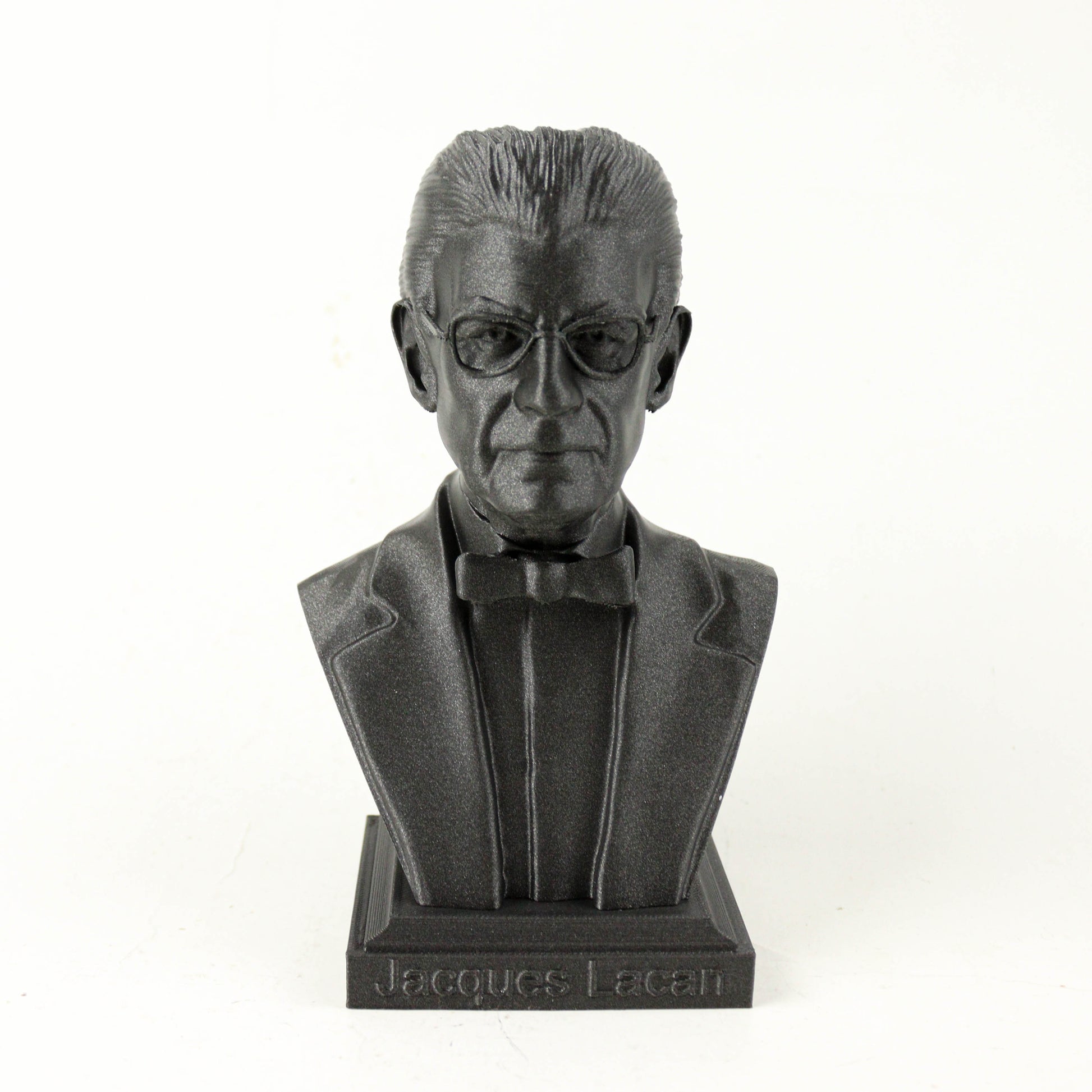 A black bust sculpture of a man wearing a suit and bow tie, with the name "Jacques Lacan" engraved on the base.