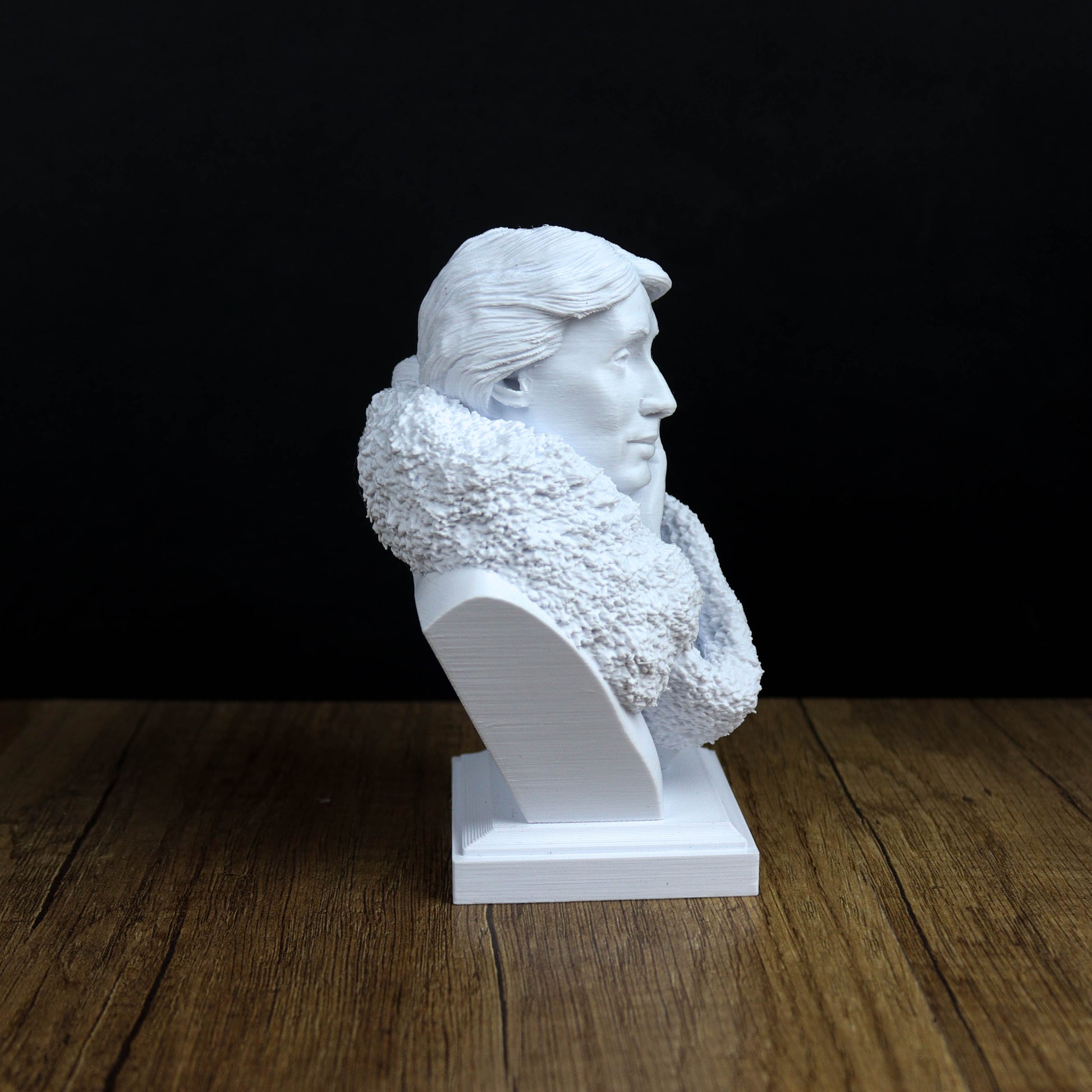 A white bust sculpture of a person's head is displayed on a wooden surface against a black background.