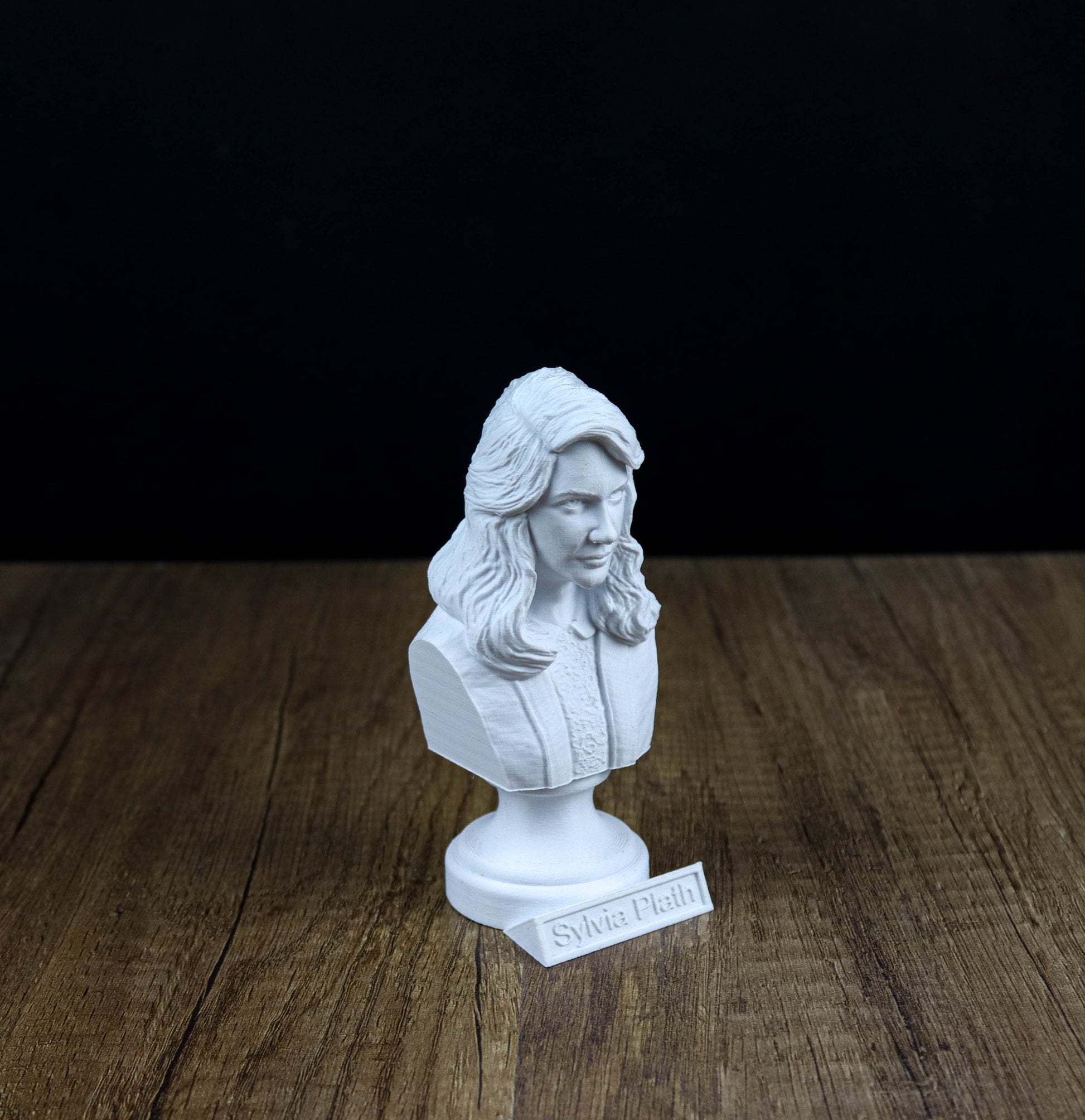 A white bust of a woman is displayed on a wooden surface, with a nameplate underneath it.