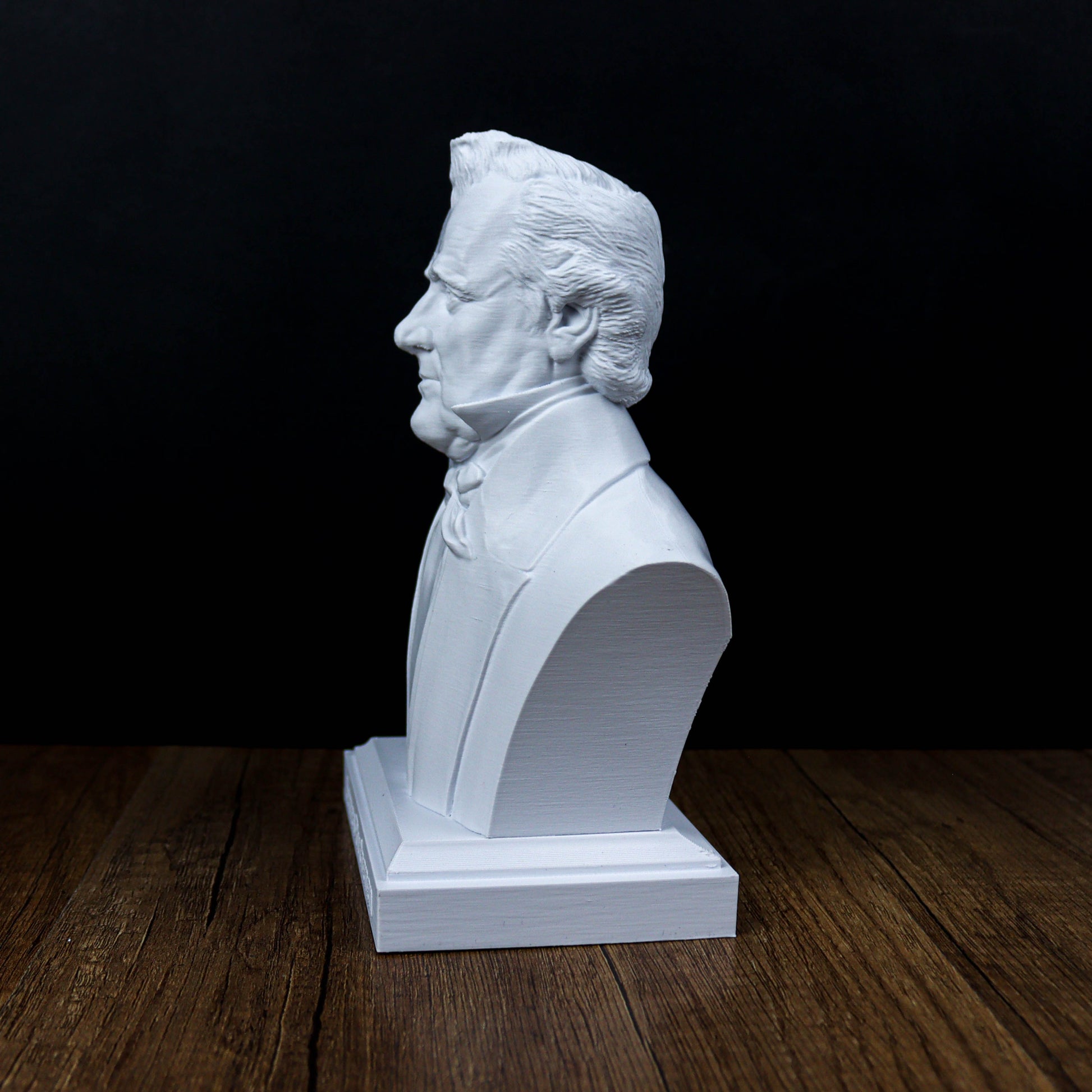 A white bust of a man is displayed on a wooden surface against a dark background.