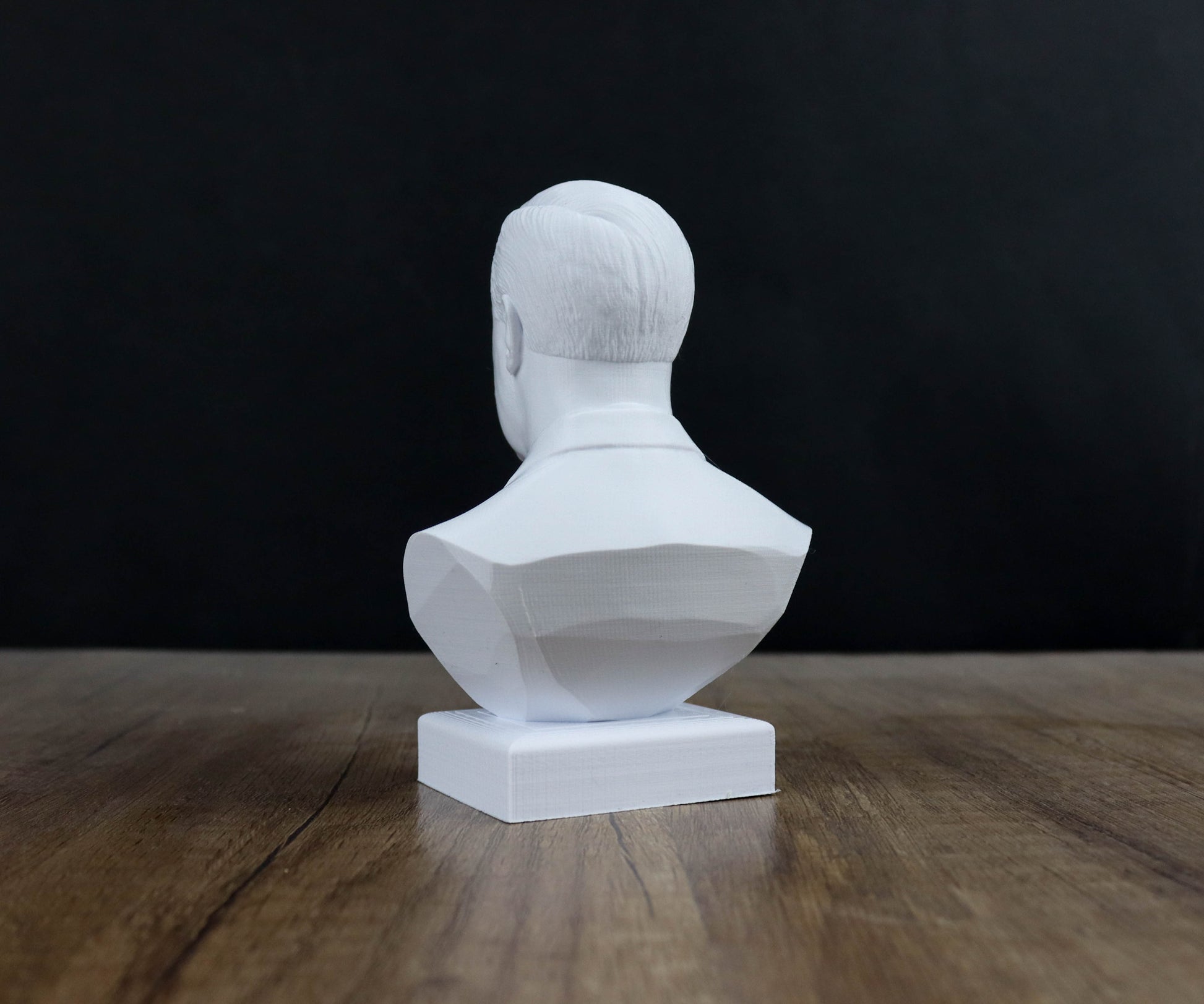 A white bust sculpture is displayed on a wooden surface against a dark background.