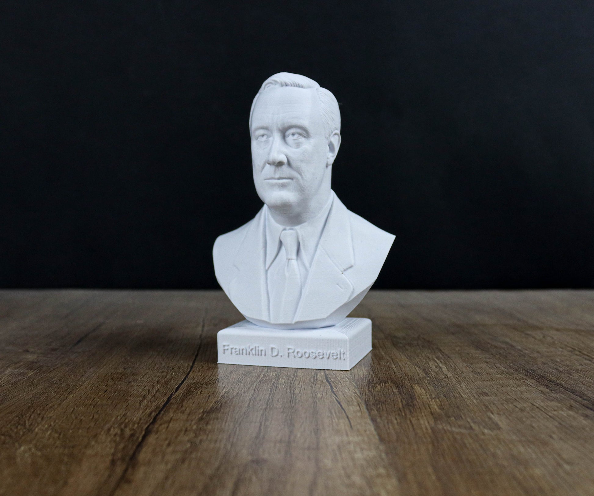 A white bust of a man wearing a suit and tie, sitting on a wooden surface.