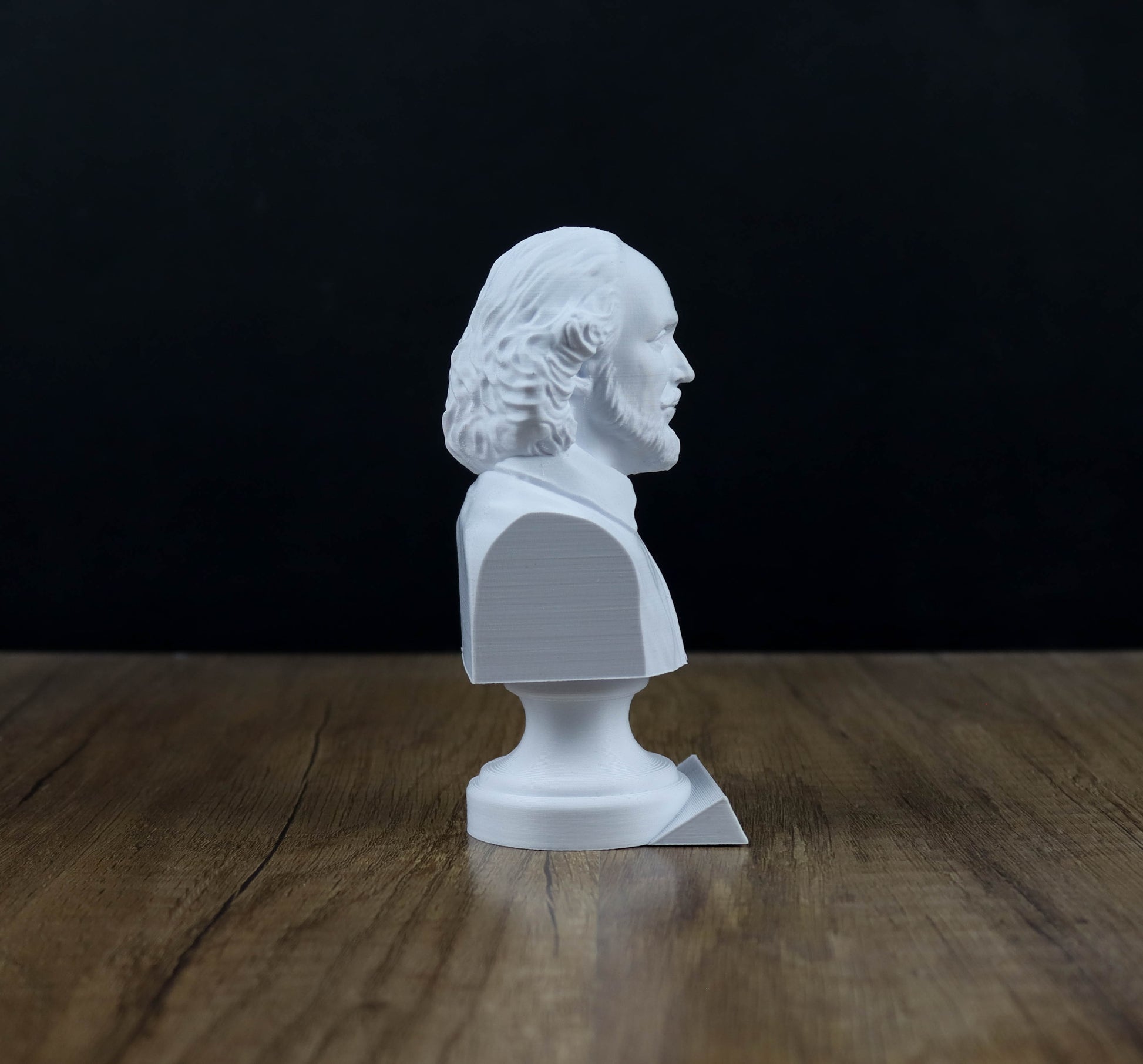 A white bust of a man is sitting on a wooden surface against a black background.