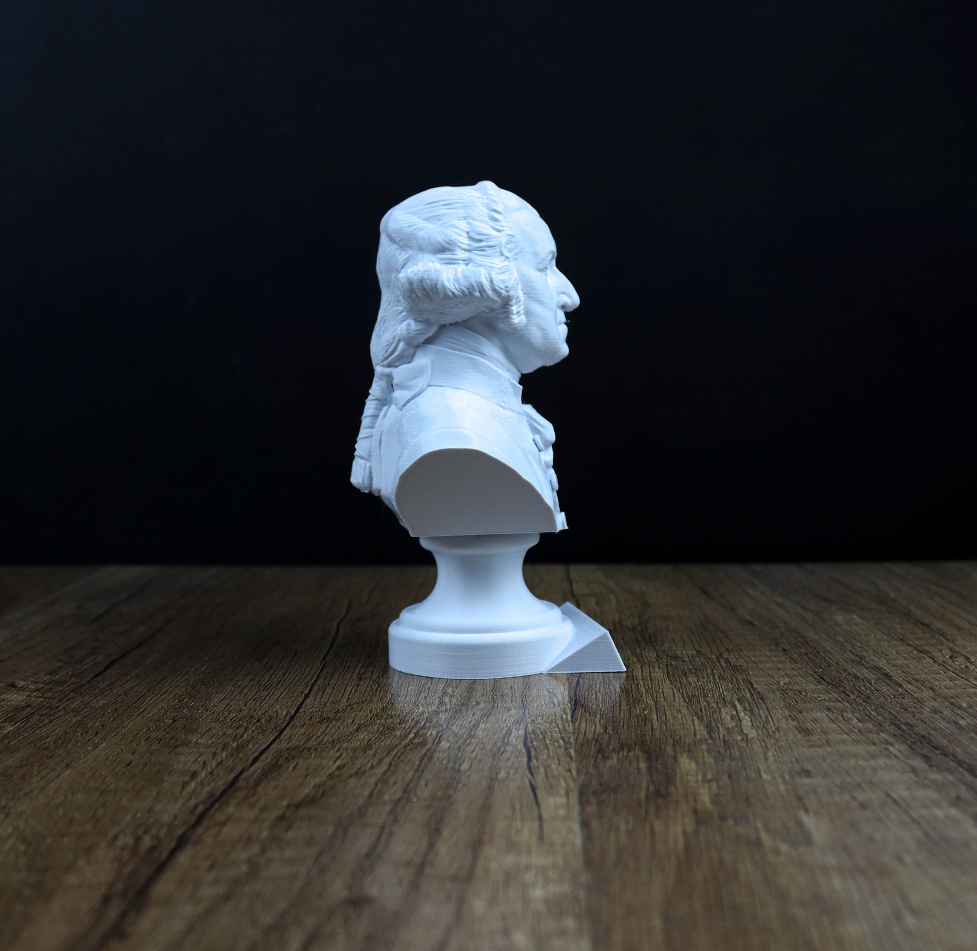 A white bust of a person is sitting on a wooden surface against a dark background.