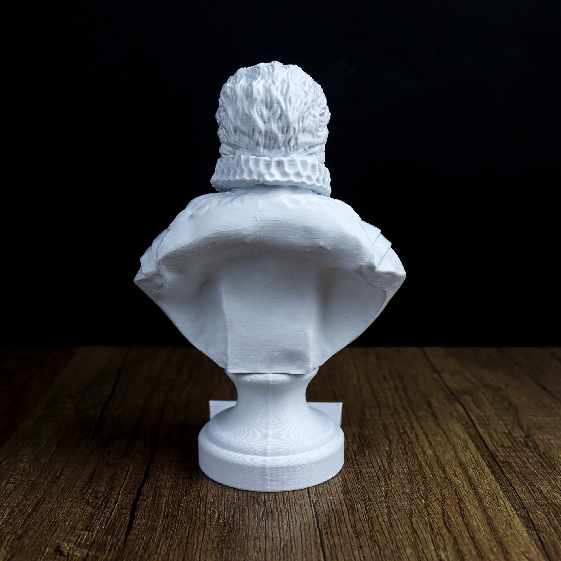 A white bust sculpture is displayed on a wooden surface against a dark background.