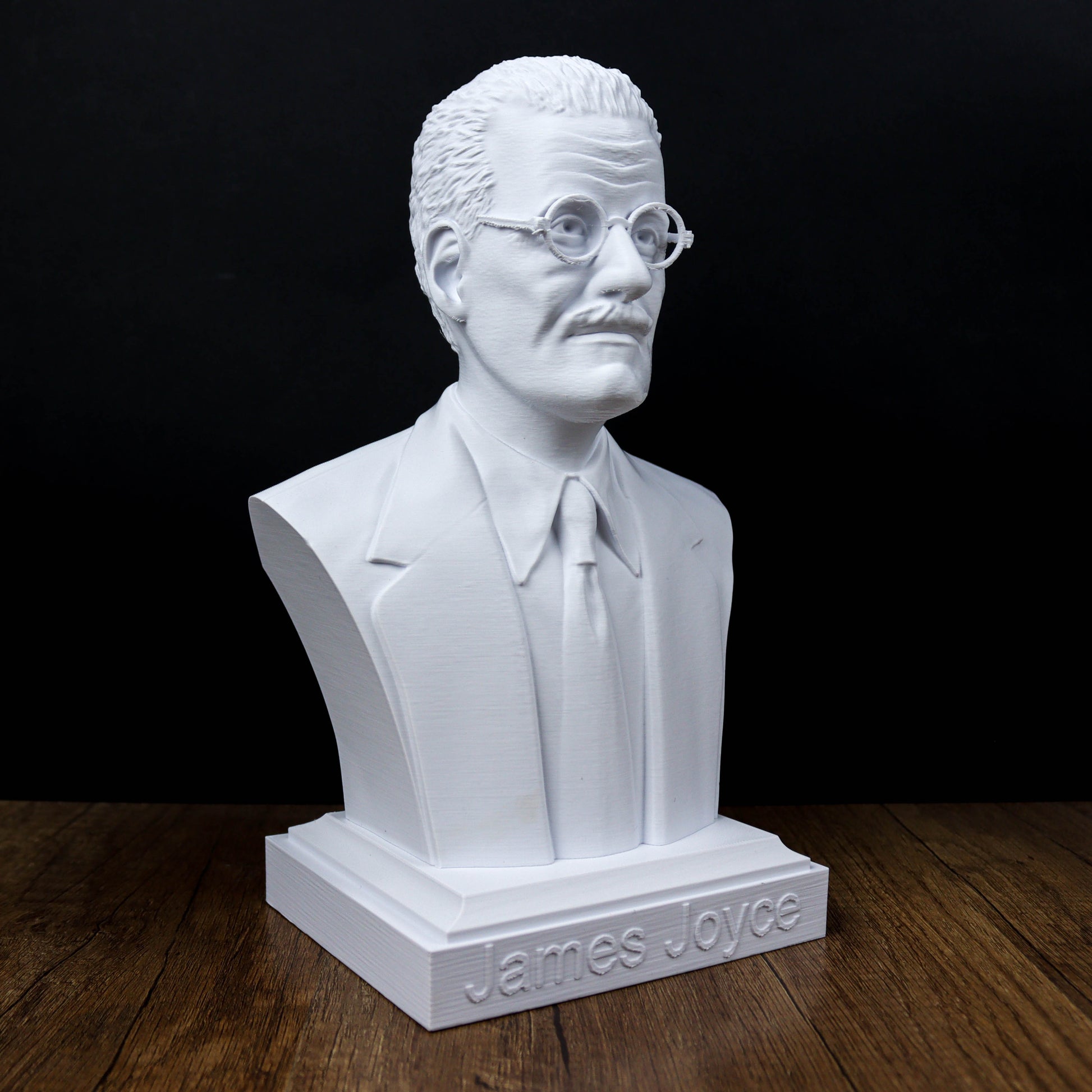 A white bust of a man wearing glasses and a suit, sitting on a wooden surface.