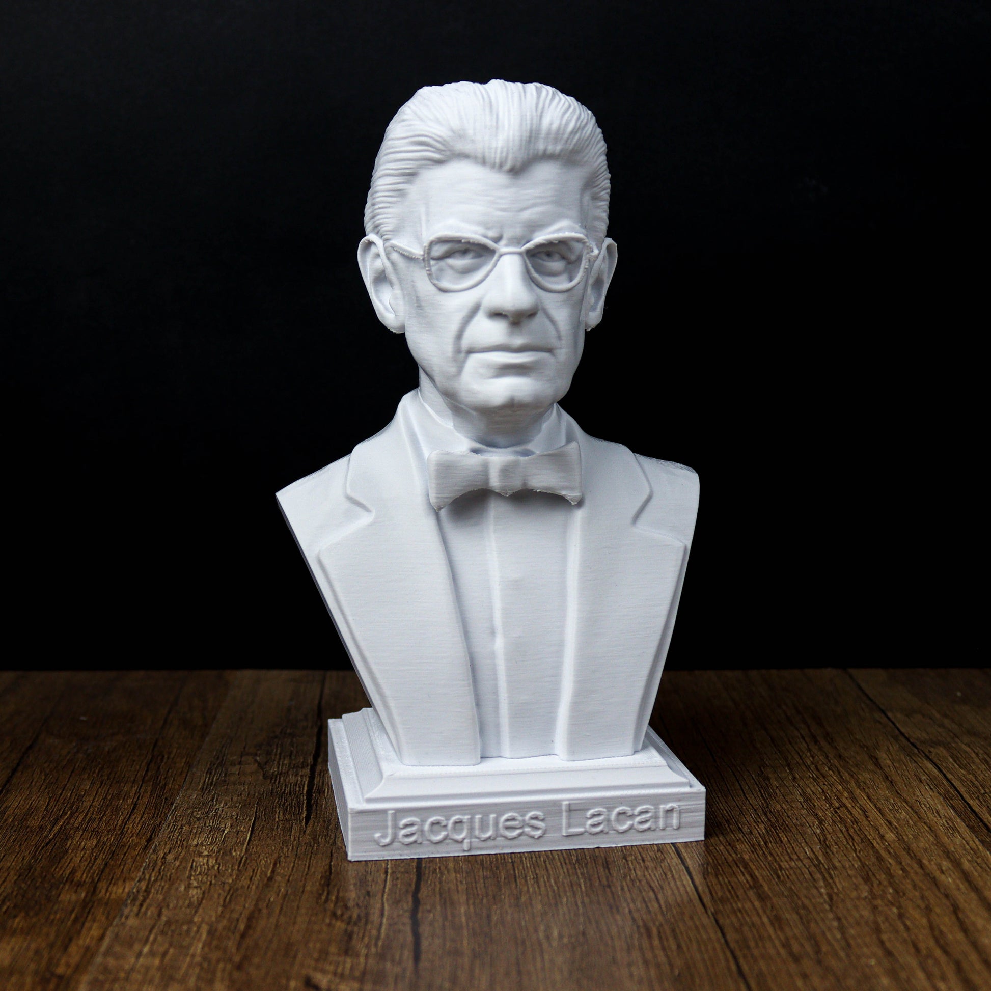A white bust of a man wearing a suit and bow tie, with the name "Jacques Lecan" written on the base.