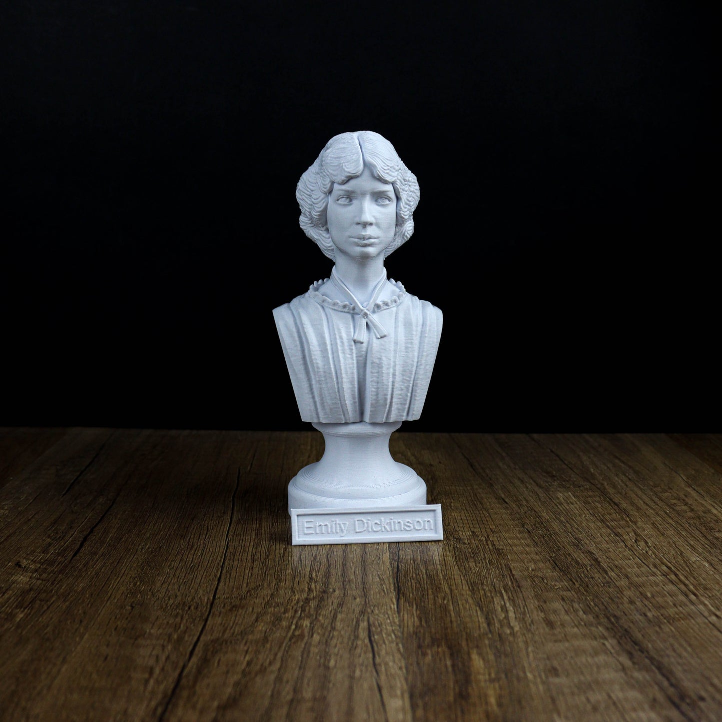 A white bust of a person, likely a historical figure, is displayed on a wooden surface against a black background.