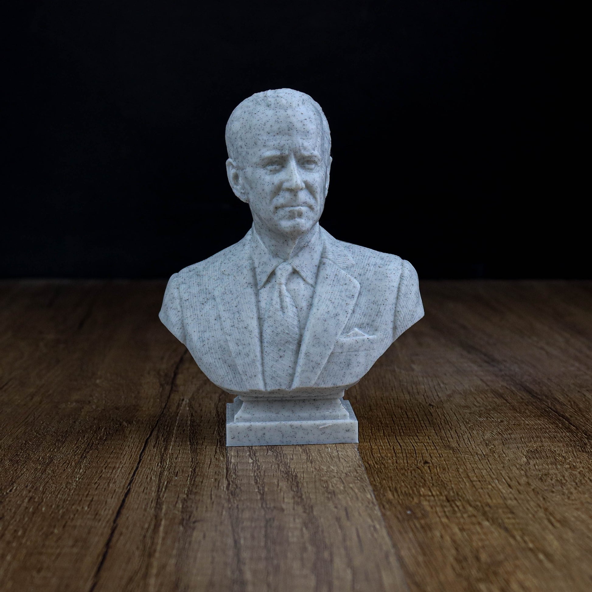 A small white bust of a man wearing a suit and tie, placed on a wooden surface.