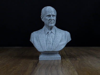 A gray stone bust of a man wearing a suit and tie, sitting on a wooden surface against a dark background.