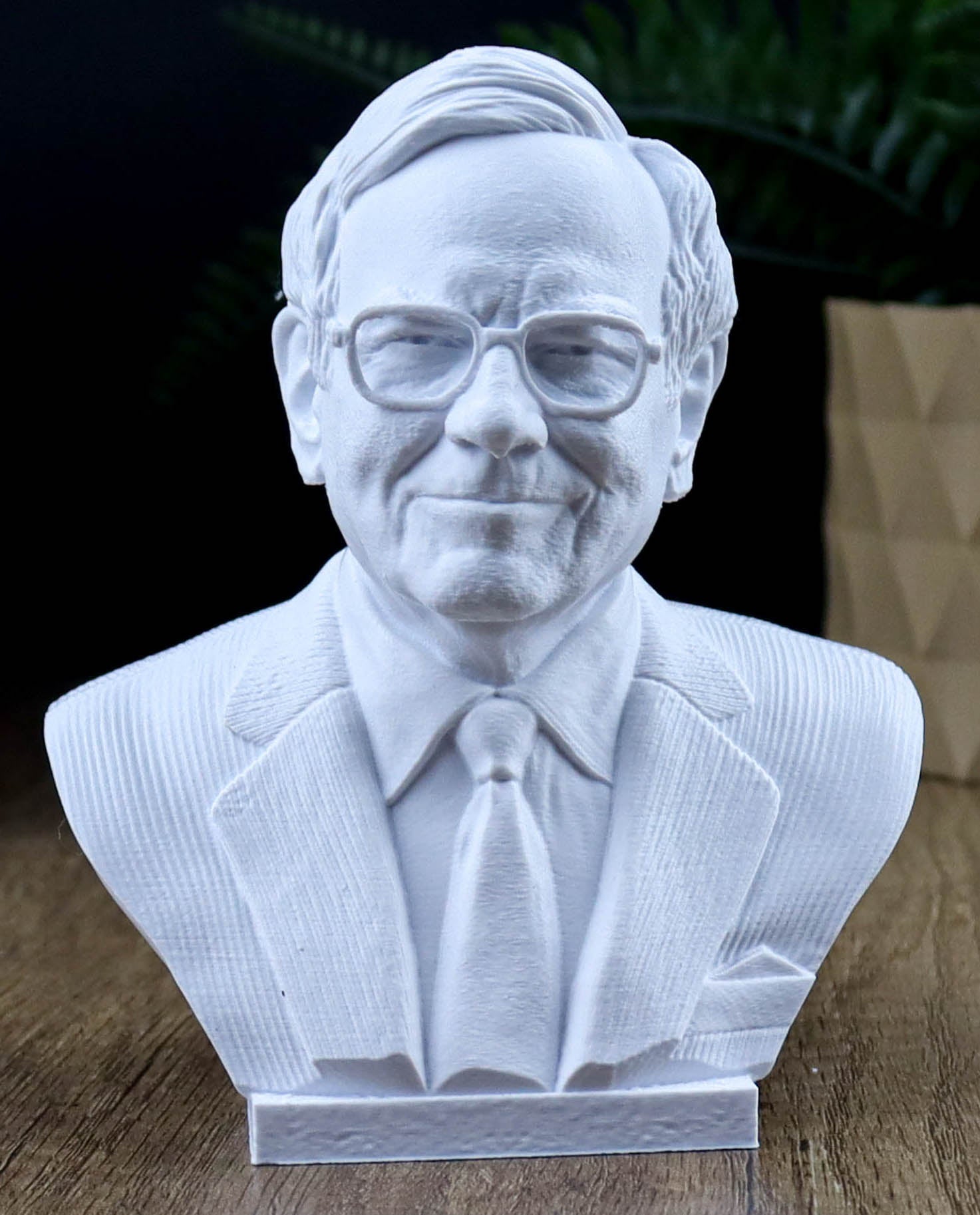 A white bust sculpture of a man wearing glasses and a suit, sitting on a wooden surface.