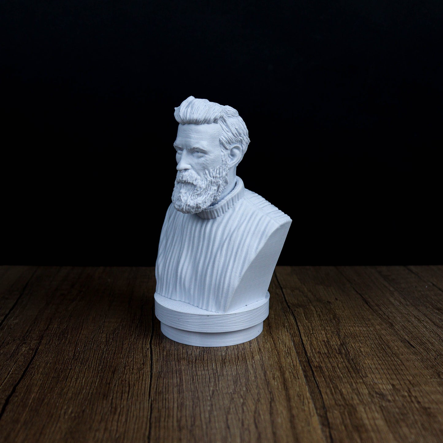 A white bust of a bearded man is displayed on a wooden surface against a dark background.