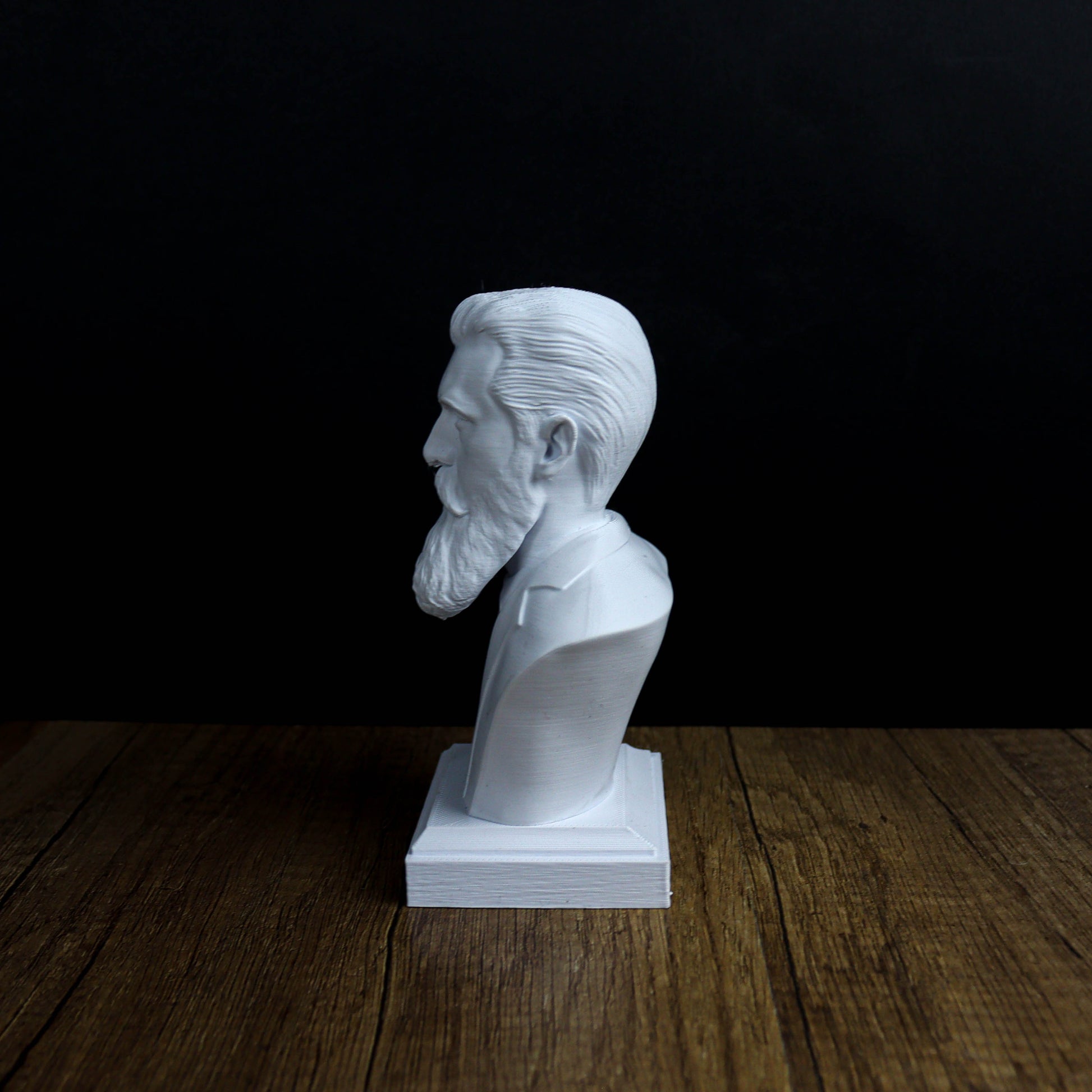 A white bust of a bearded man is displayed on a wooden surface against a black background.
