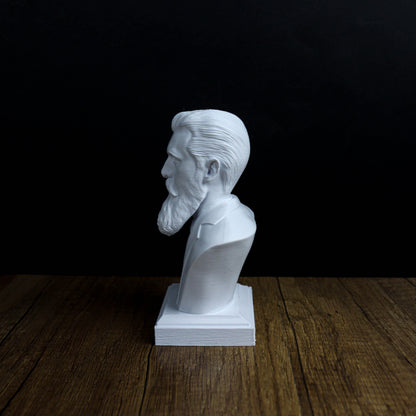 A white bust of a bearded man is displayed on a wooden surface against a black background.