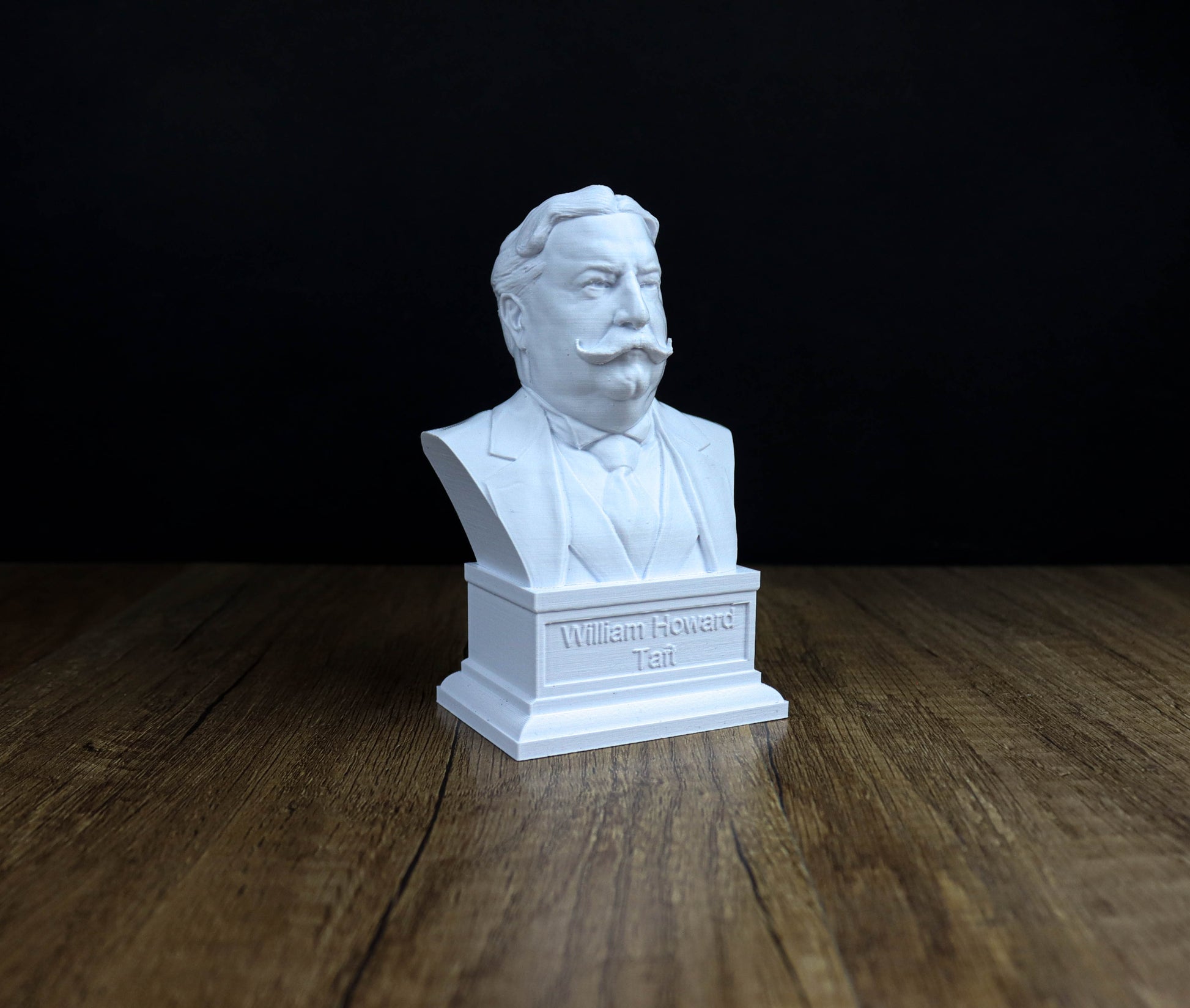 A white bust of a man with a mustache and a suit, sitting on a wooden surface.
