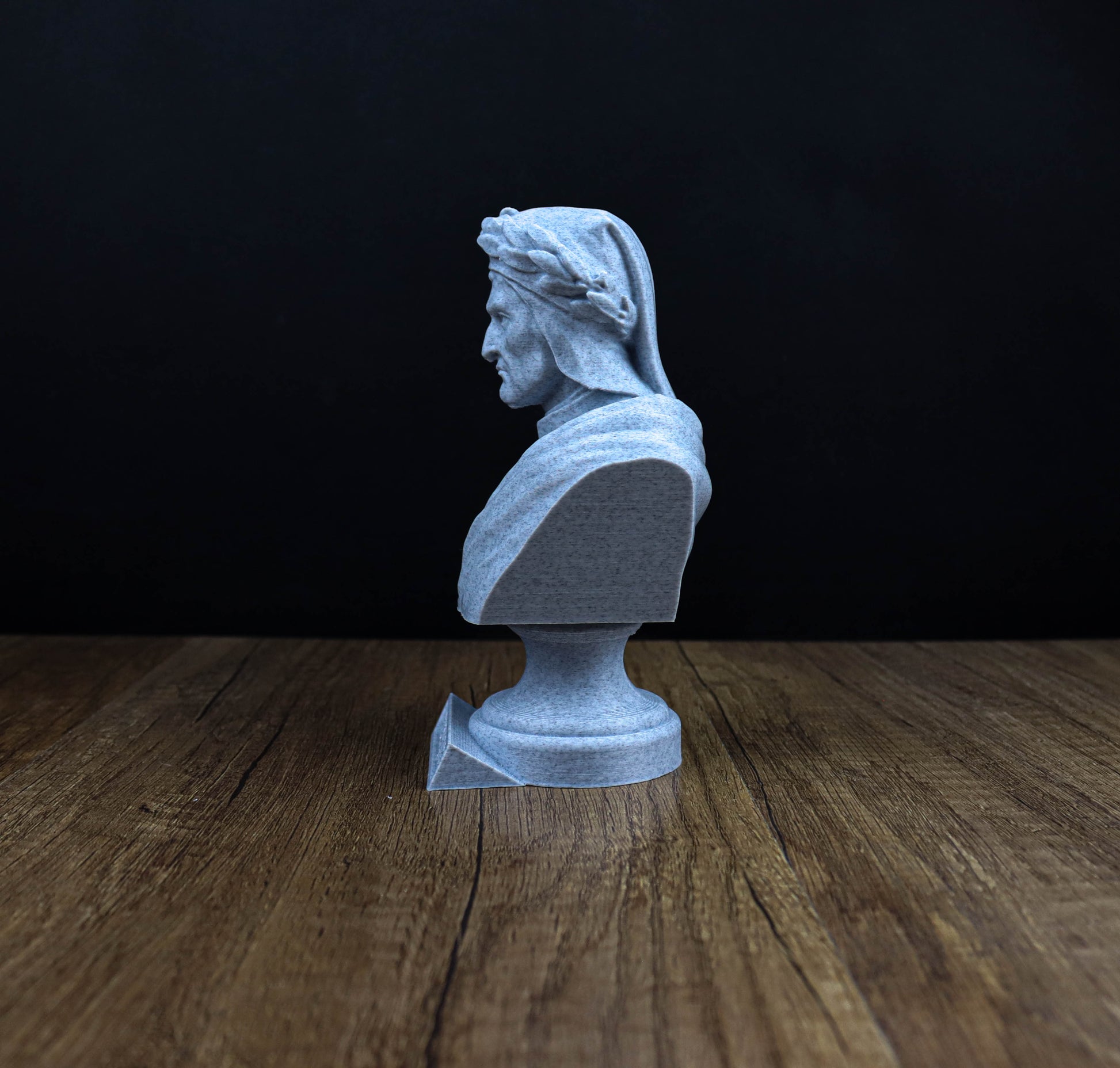 A white bust of a man is displayed on a wooden surface against a dark background.