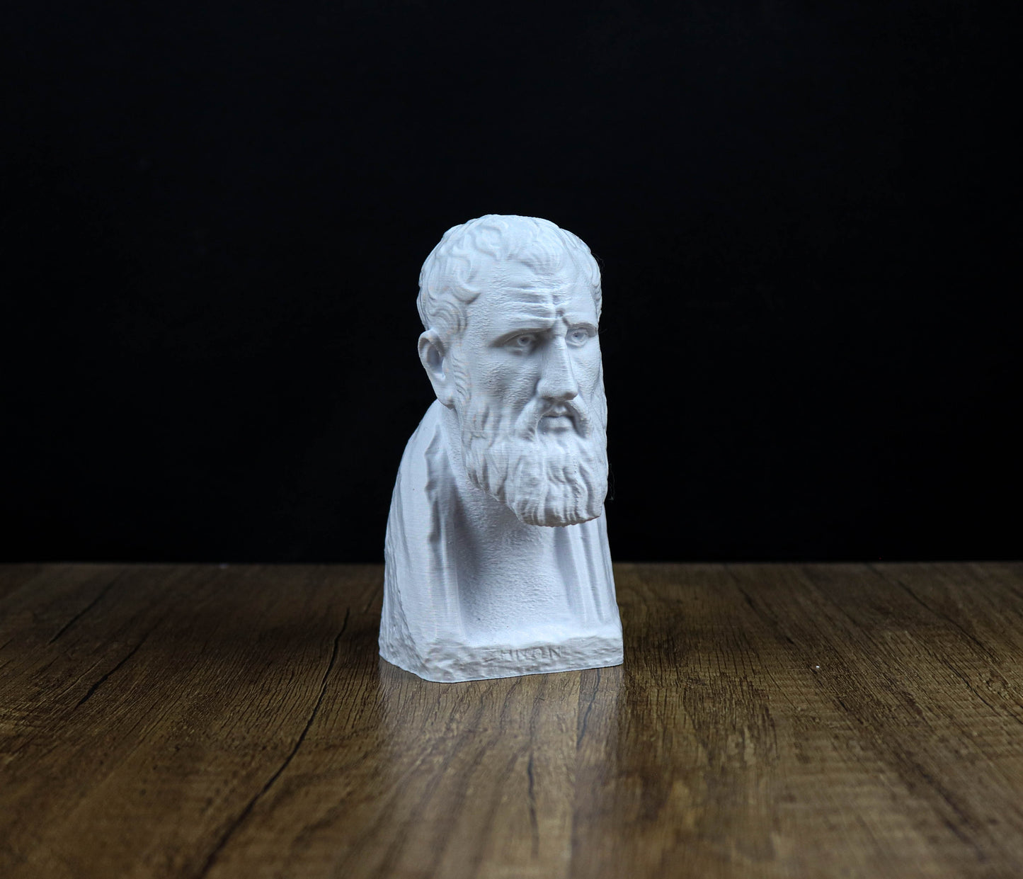A white bust of a bearded man is displayed on a wooden surface against a black background.