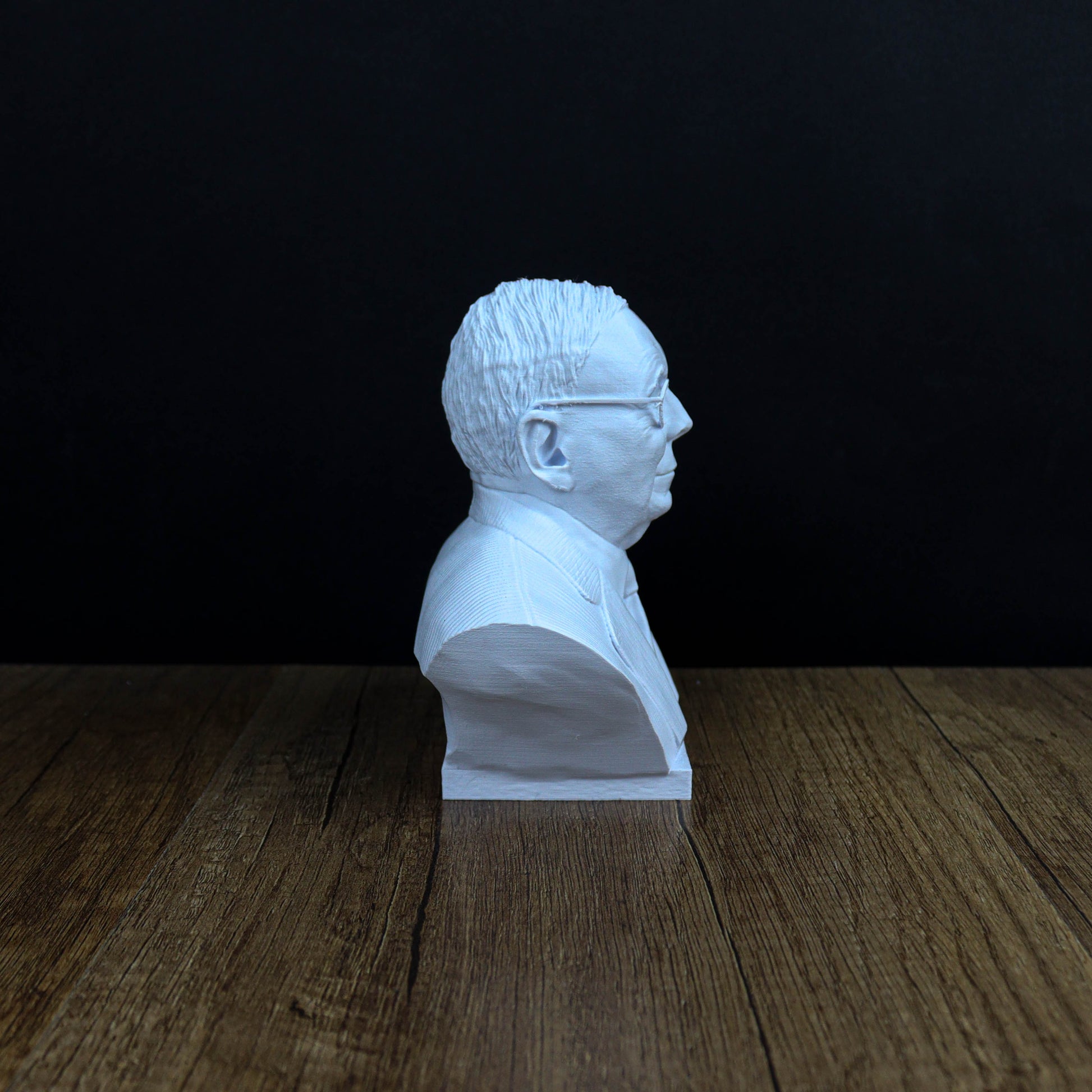 A white bust of a man's head is sitting on a wooden surface against a dark background.