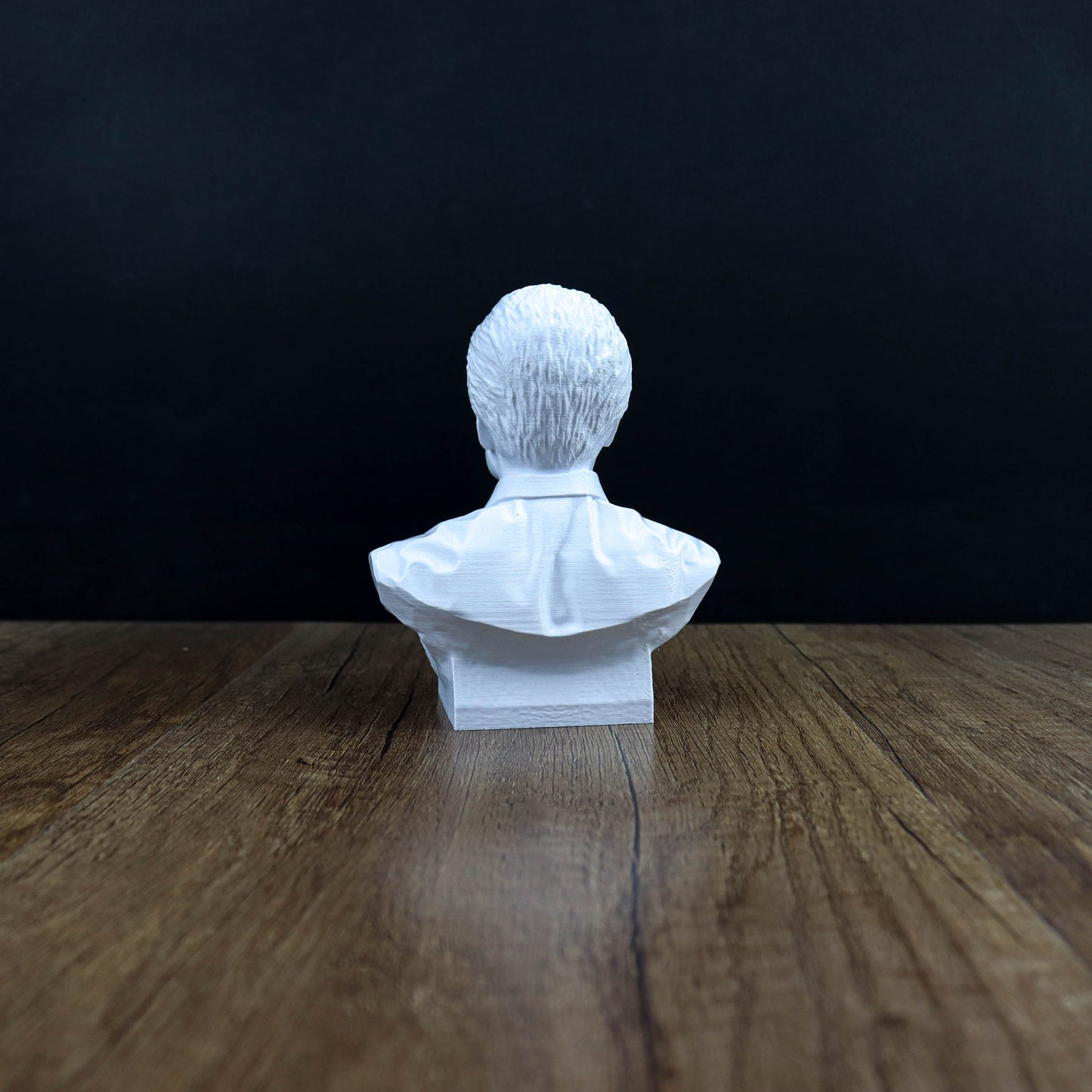 A white bust of a person sitting on a wooden surface against a dark background.