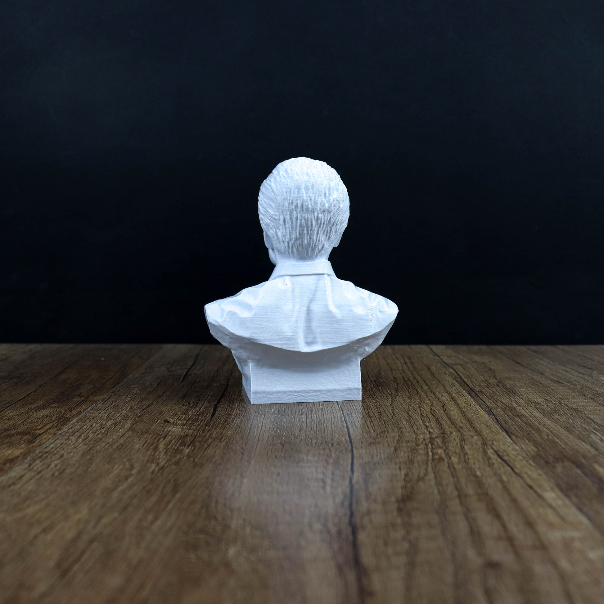 A white bust of a person sitting on a wooden surface against a dark background.