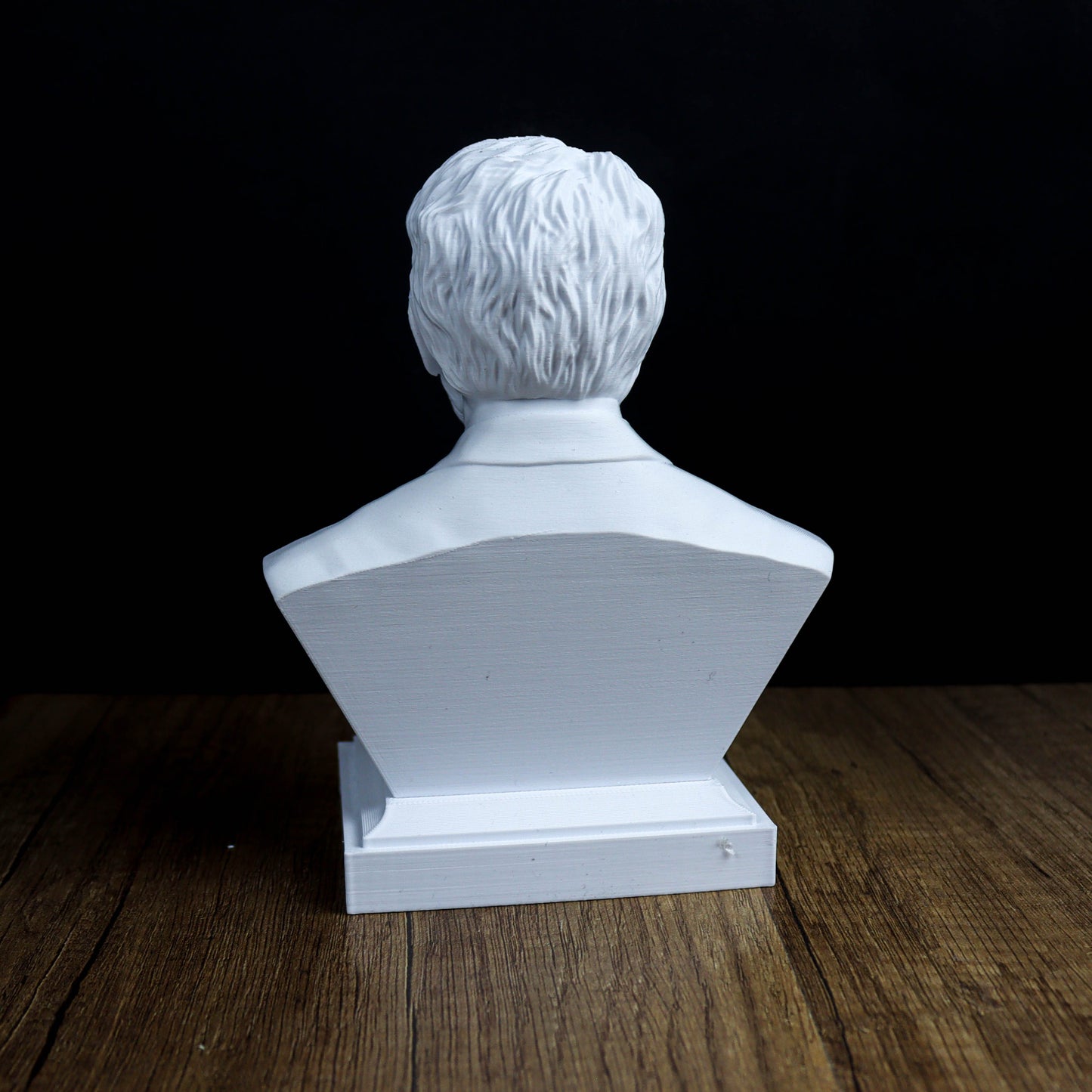 A white bust sculpture of a person's head is displayed on a wooden surface against a black background.