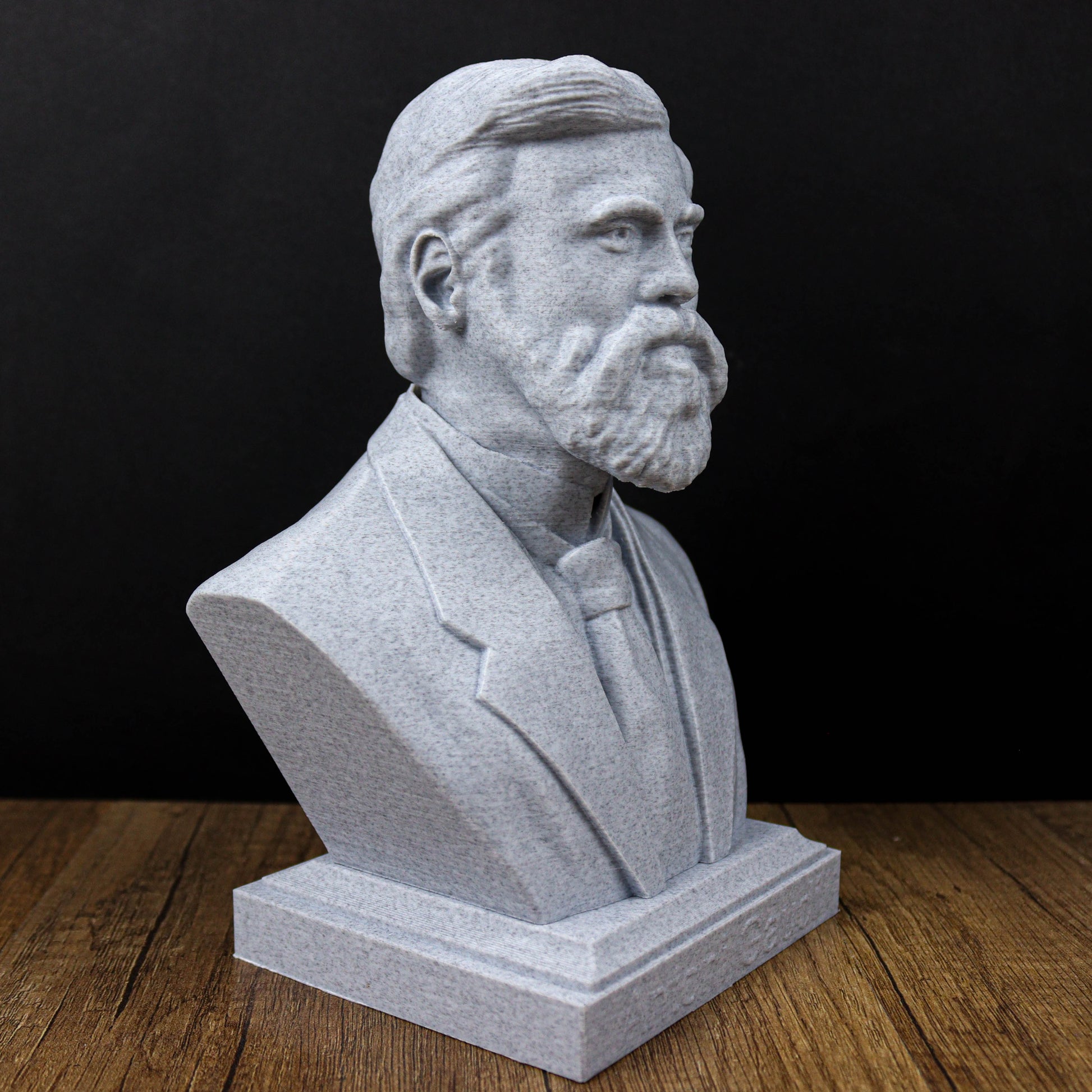 A gray stone bust of a man with a beard, wearing a suit and tie, sitting on a wooden surface.