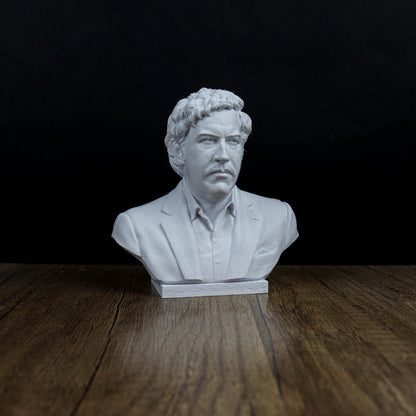 A white bust of a man with curly hair and a mustache, wearing a suit, is displayed on a wooden surface against a dark background.