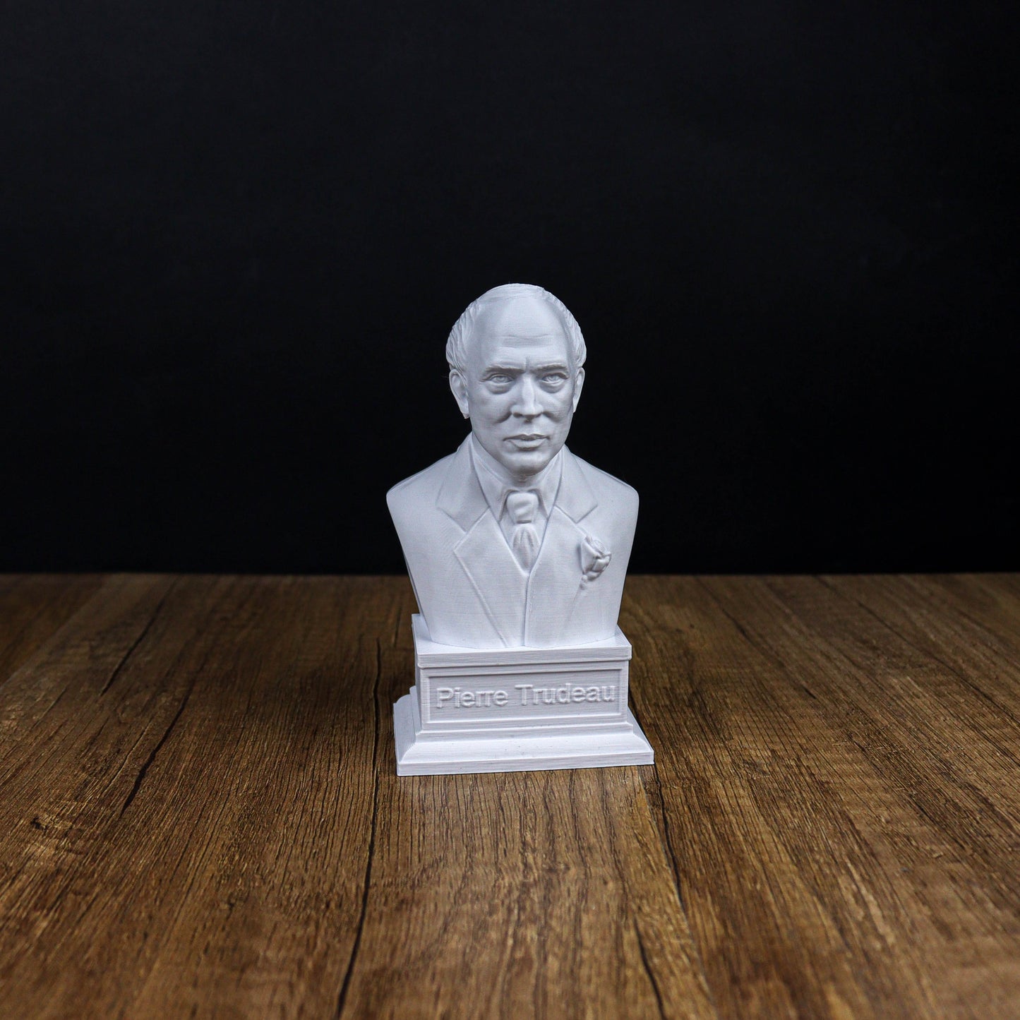 A white bust of a man wearing a suit and tie, placed on a wooden surface against a black background.