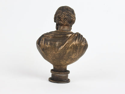 A bronze bust of a person facing away from the camera, with a draped cloth draped over the shoulders.