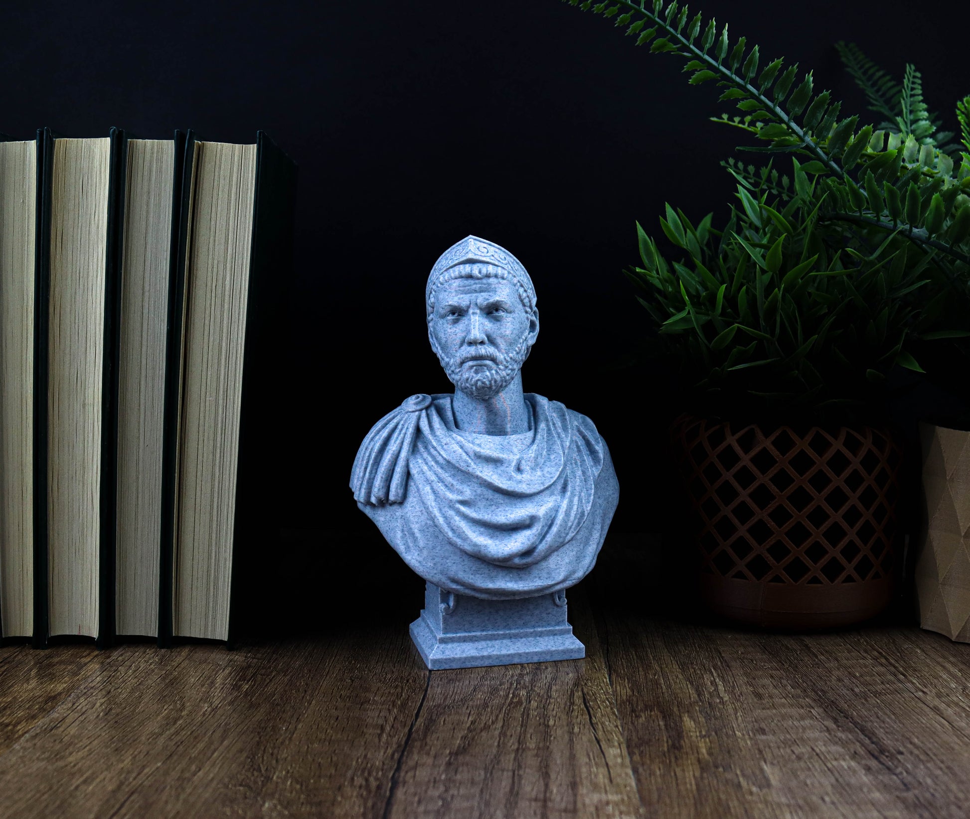 A gray bust of a man is displayed on a wooden surface, surrounded by books and a potted plant.