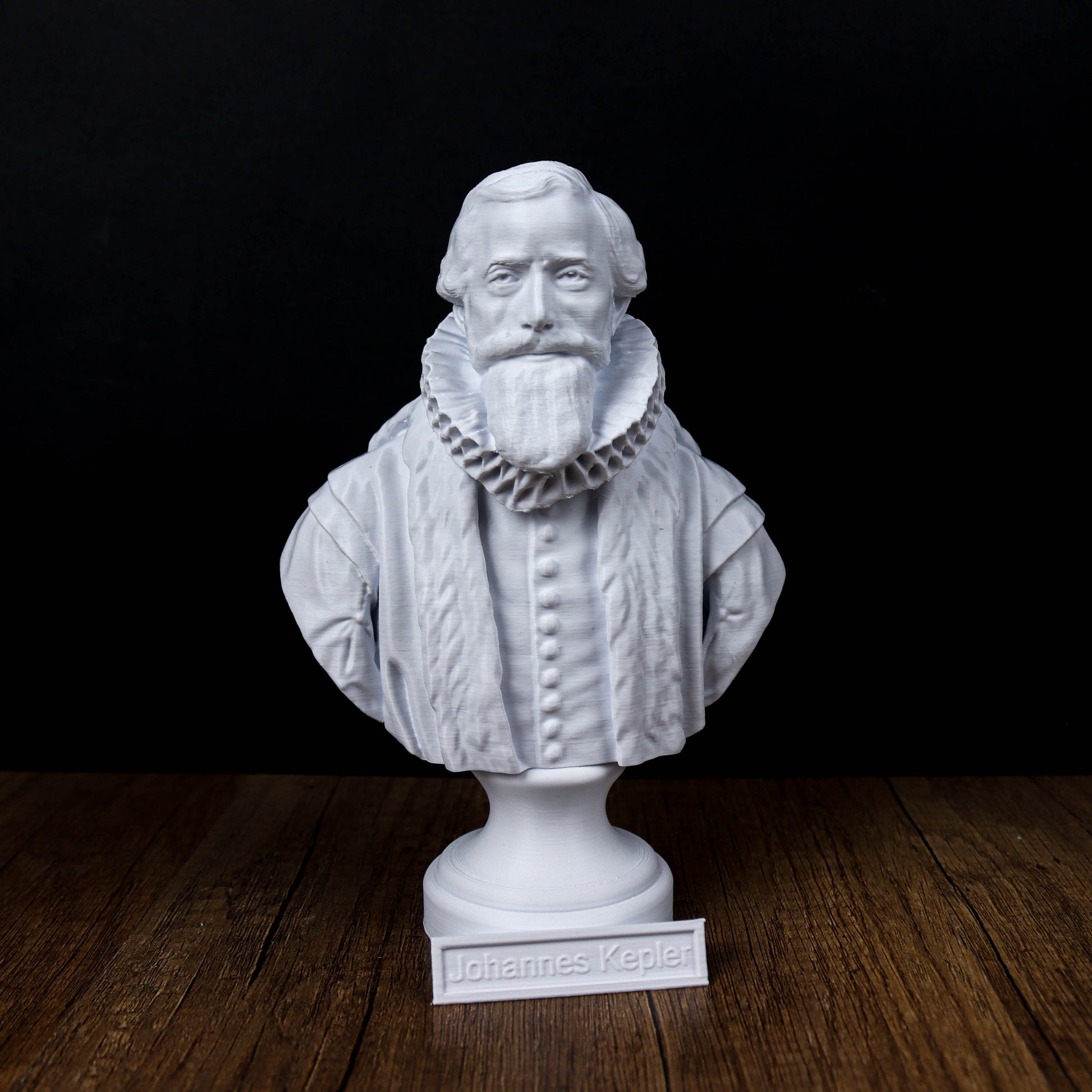 A white bust of a bearded man wearing a ruffled collar, standing on a wooden surface.