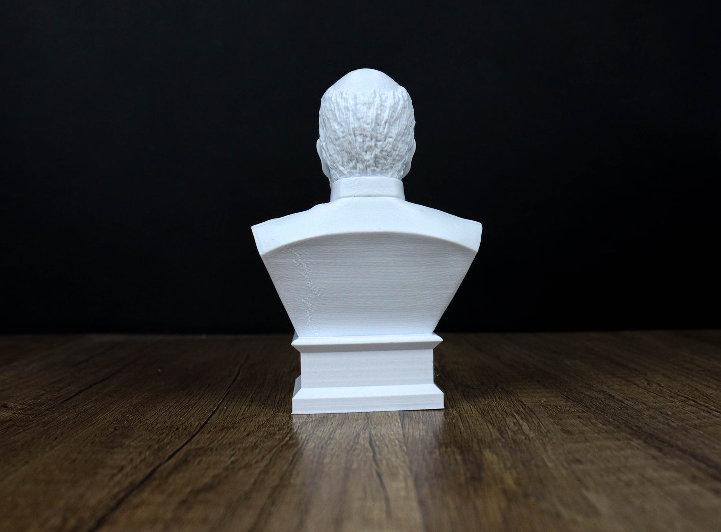 A white bust of a person is displayed on a wooden surface against a black background.