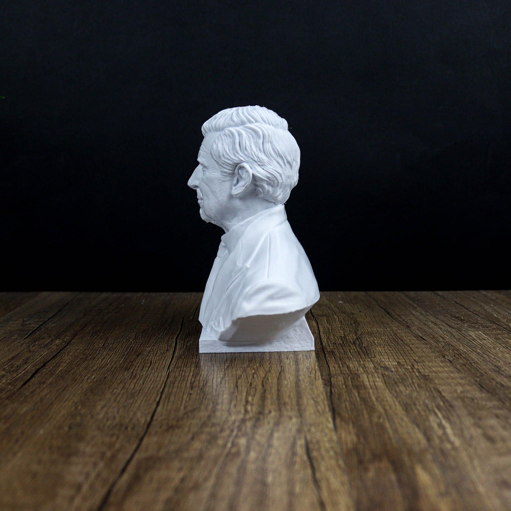 A white bust of a man is displayed on a wooden surface against a dark background.