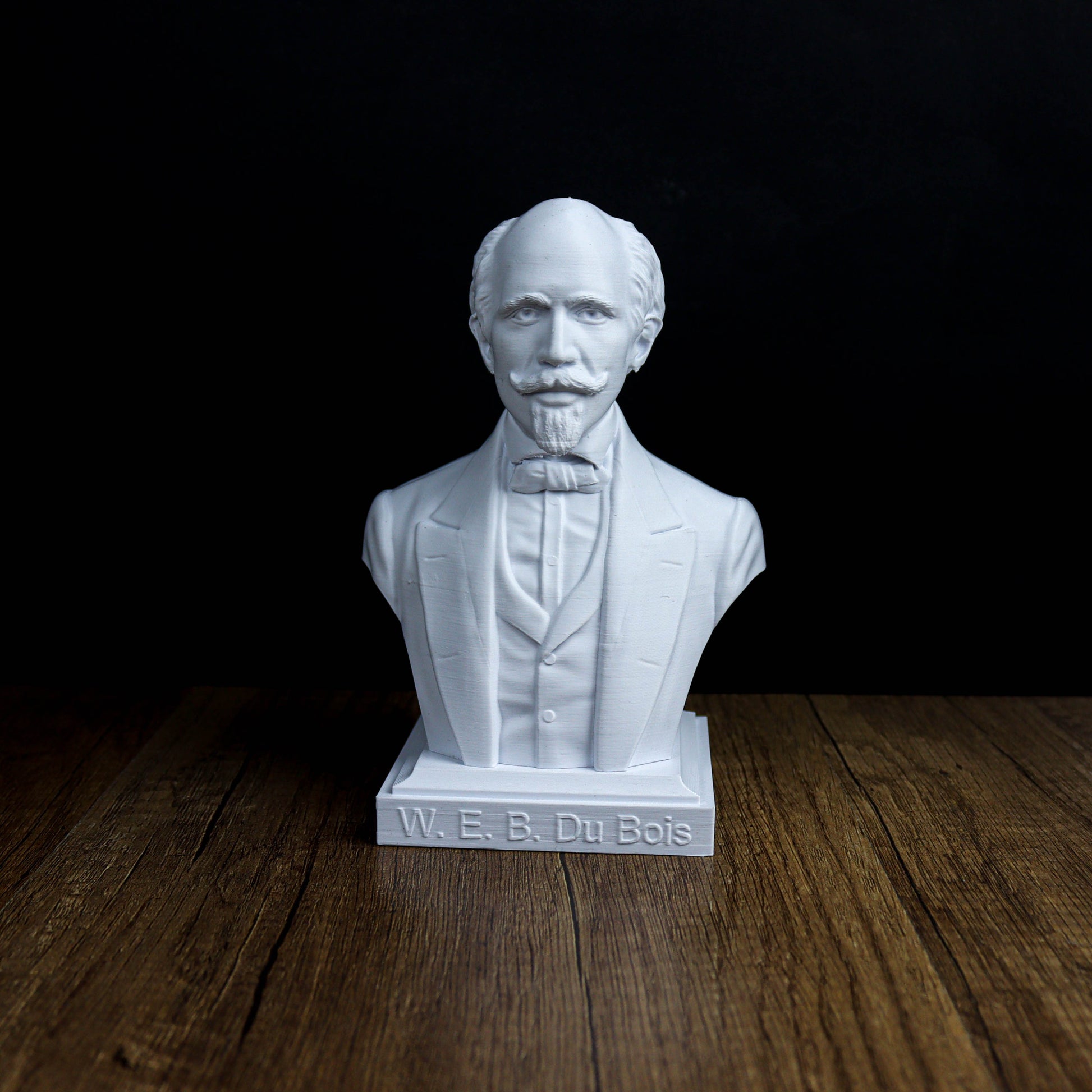 A white bust of a man with a mustache and a formal suit, standing on a wooden surface.