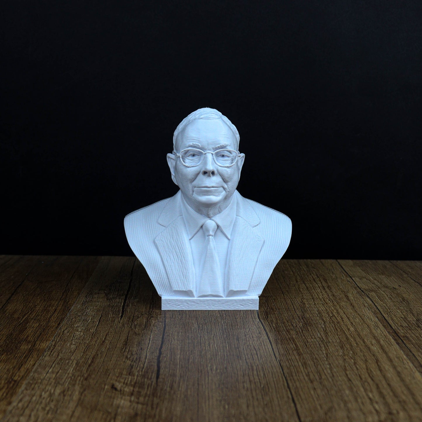 A white bust of a man wearing a suit and tie, sitting on a wooden surface against a black background.