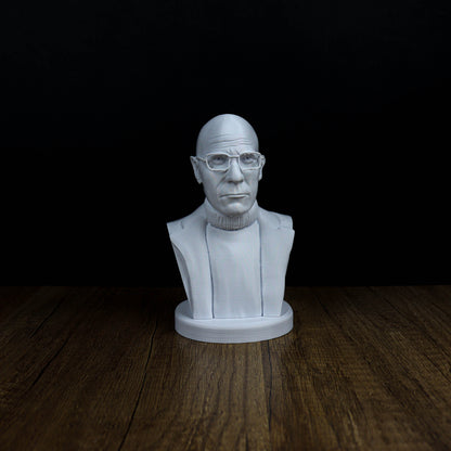 A white bust of a man wearing glasses is displayed on a wooden surface against a black background.