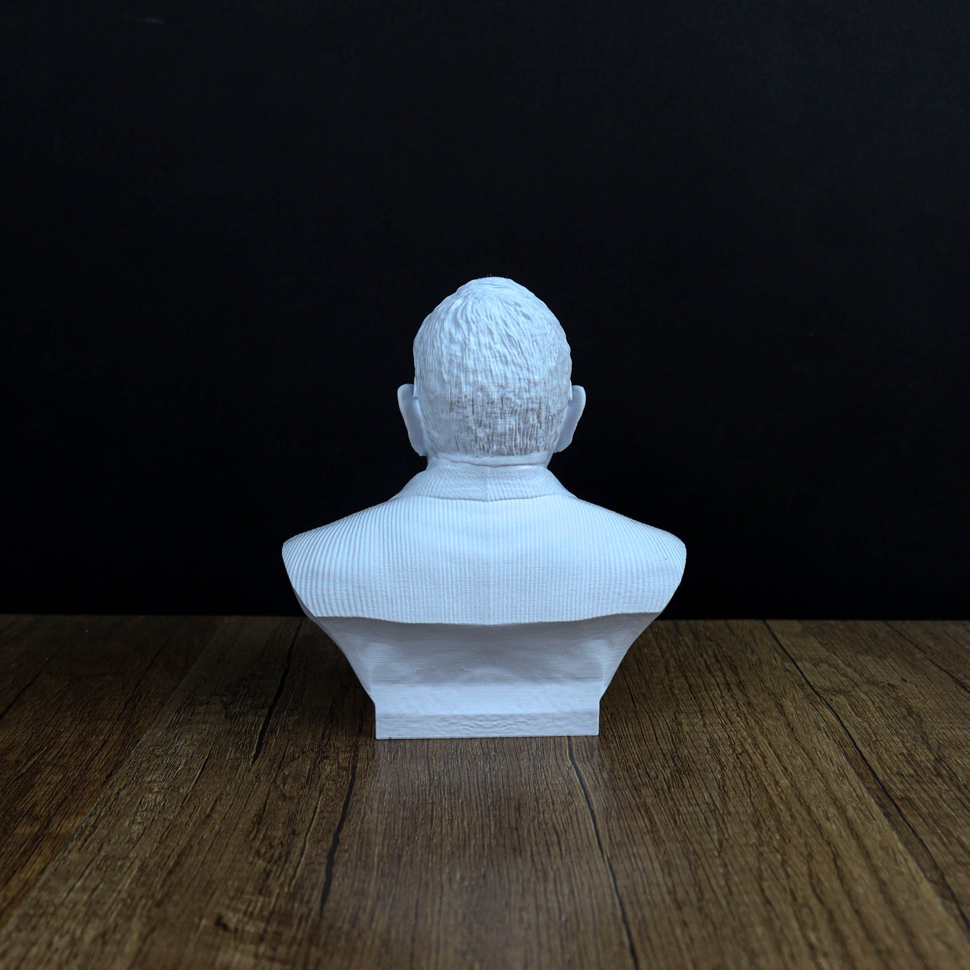 A white bust of a person's head is displayed on a wooden surface against a black background.