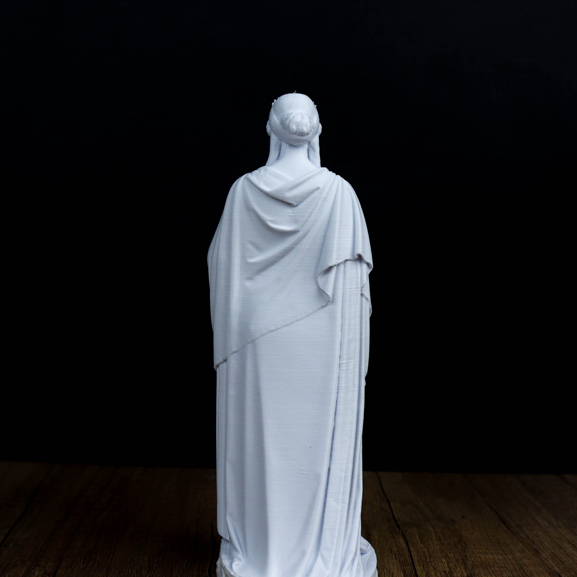 A white statue of a person standing on a wooden floor against a black background.