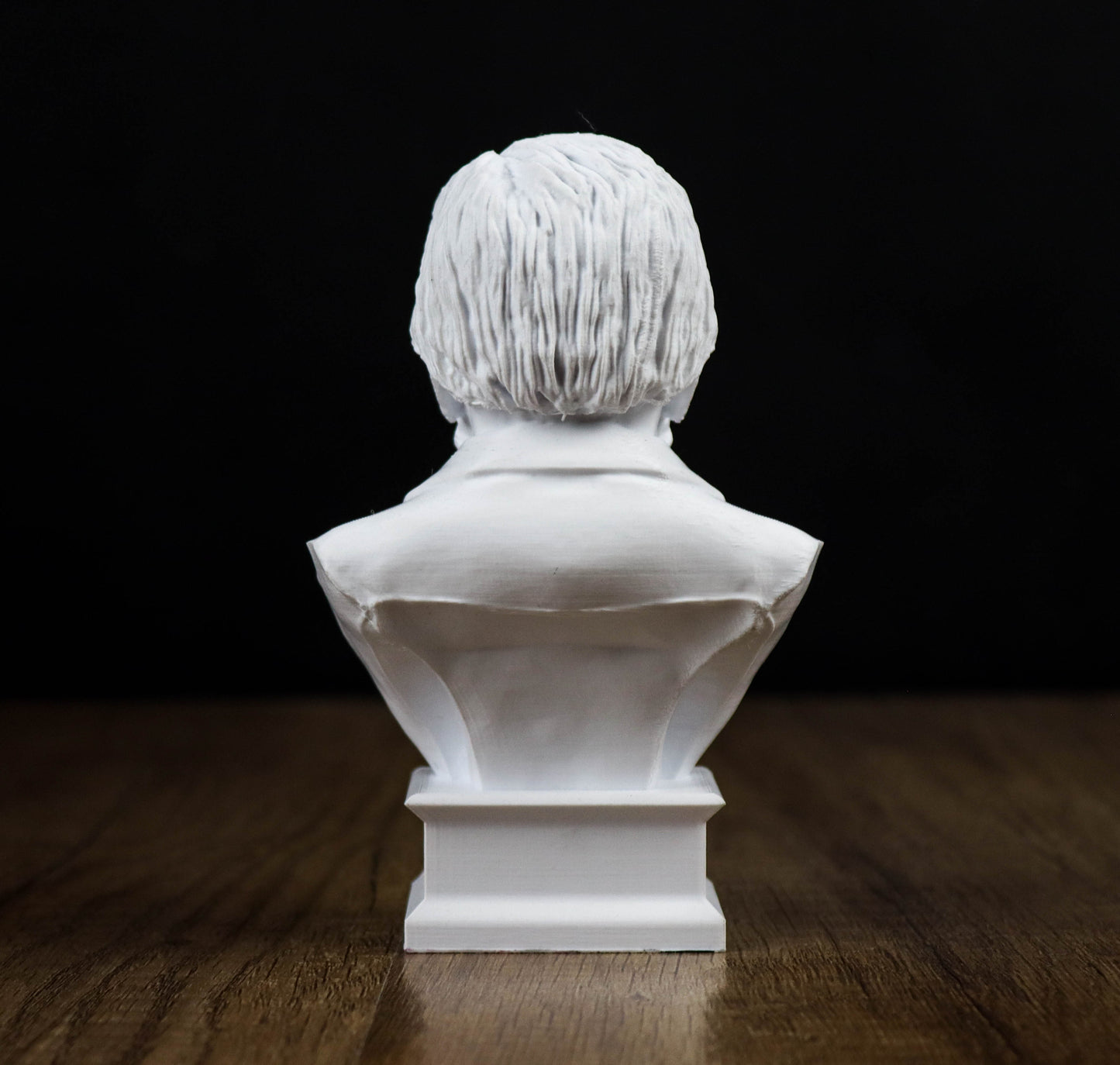 A white bust sculpture of a person's head is displayed on a wooden surface against a black background.