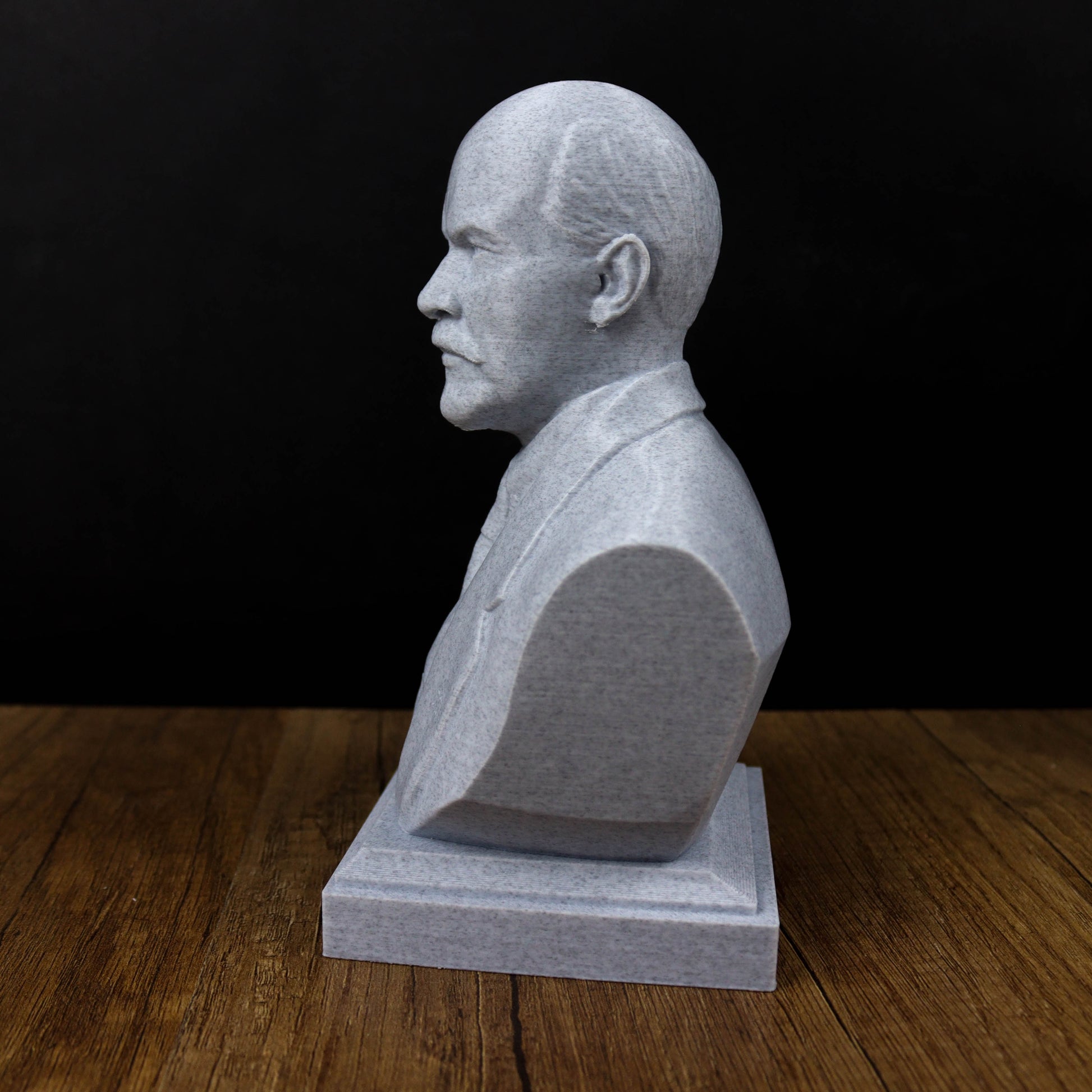 A gray stone bust of a man's head is displayed on a wooden surface against a black background.