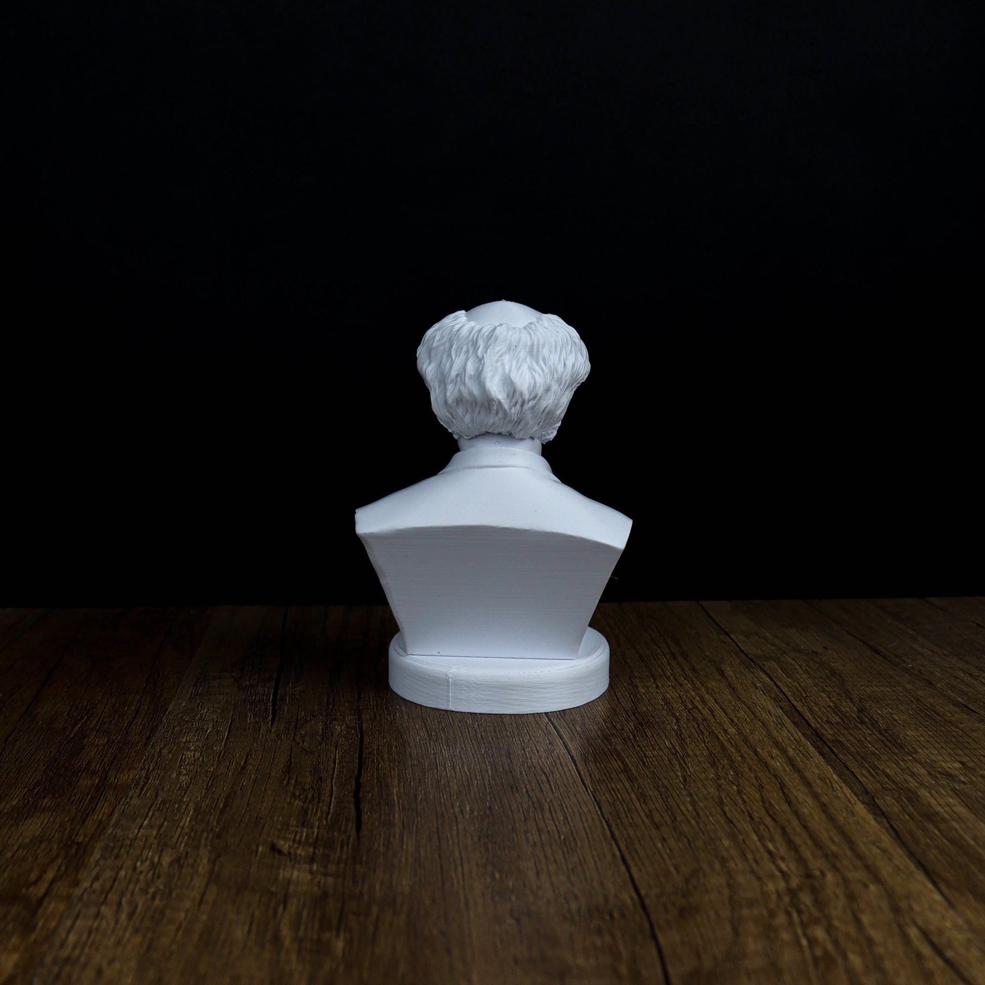 A white bust of a person is sitting on a wooden surface against a black background.
