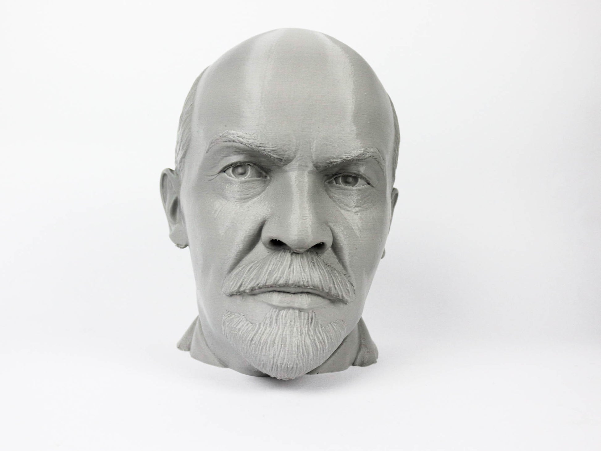 A black and white image of a man's head, possibly a bust, with a serious expression on his face.