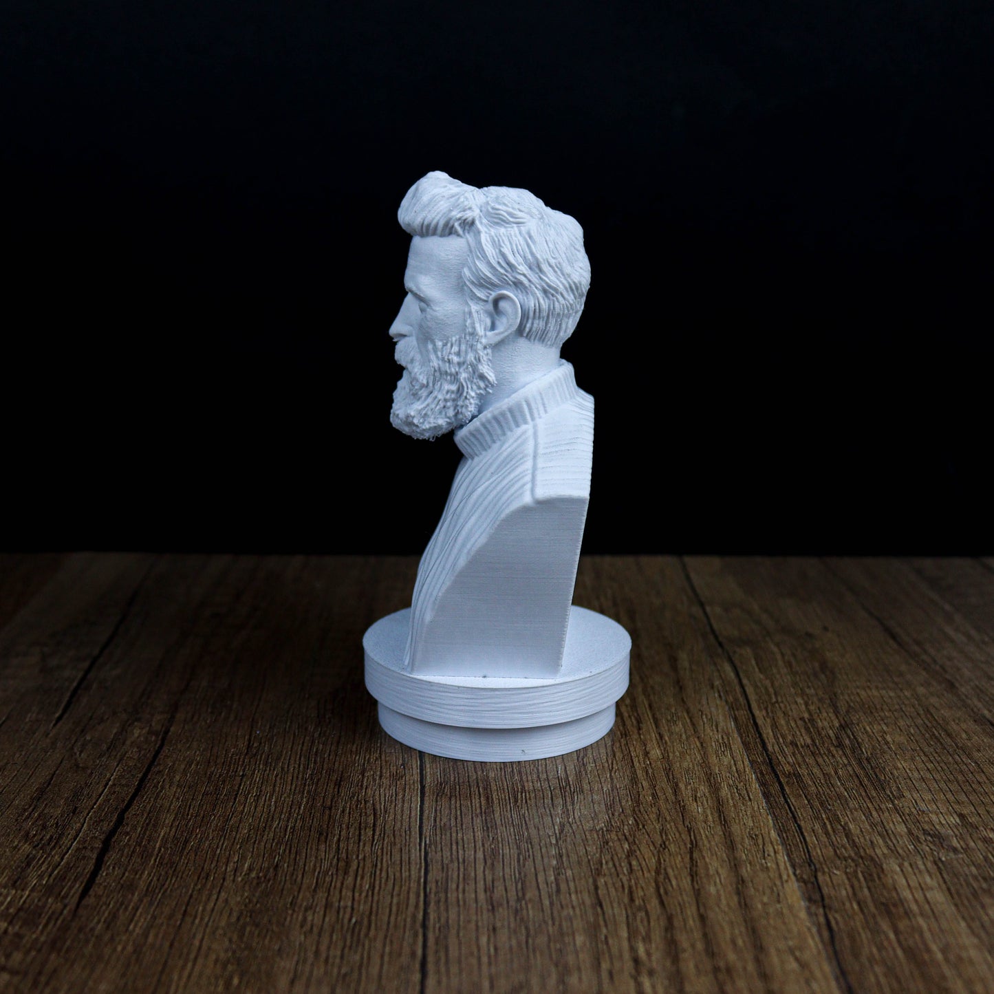 A white bust of a bearded man is displayed on a wooden surface against a dark background.