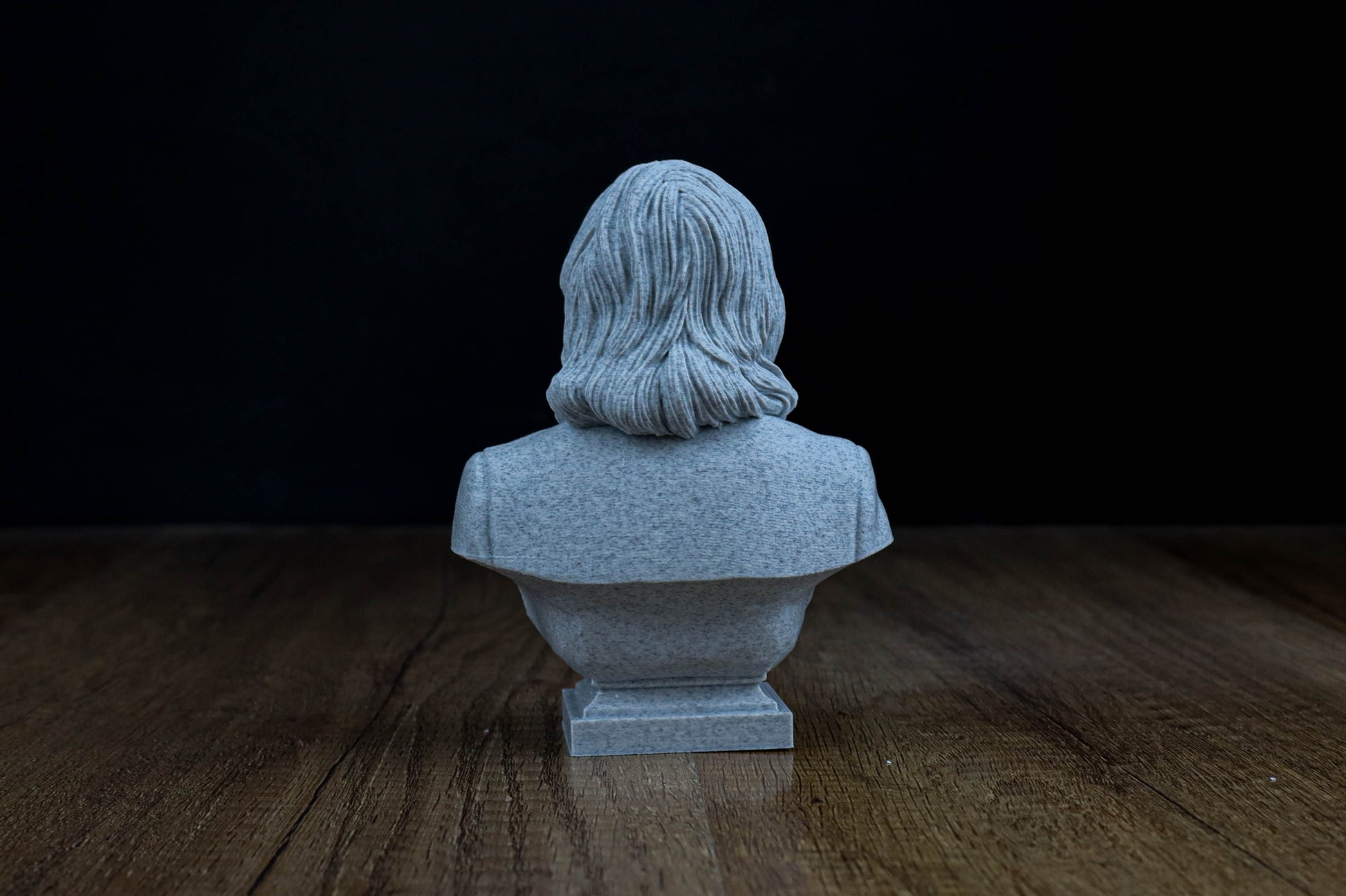A small gray stone bust of a person sitting on a wooden surface against a dark background.