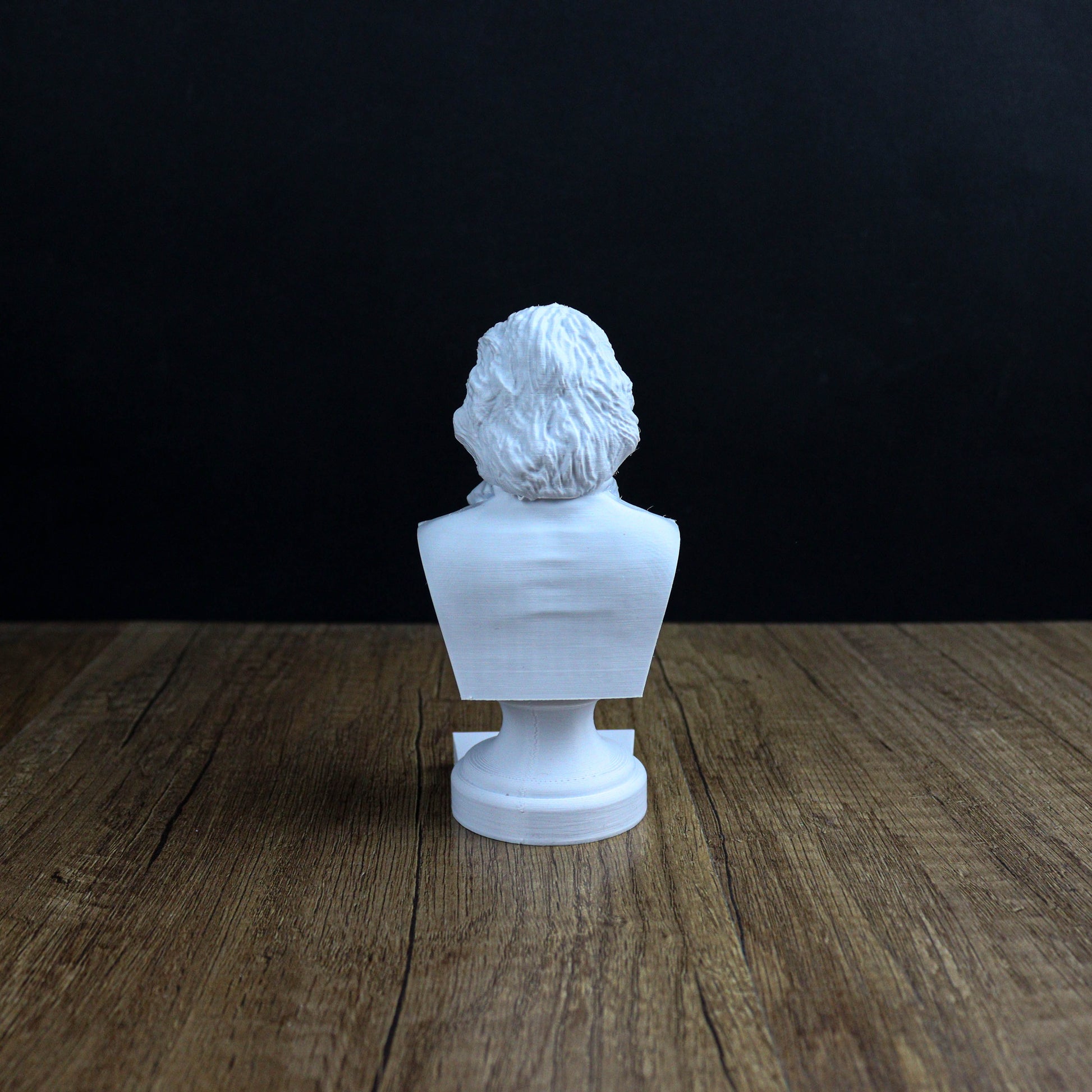 A white bust of a person is sitting on a wooden surface against a dark background.