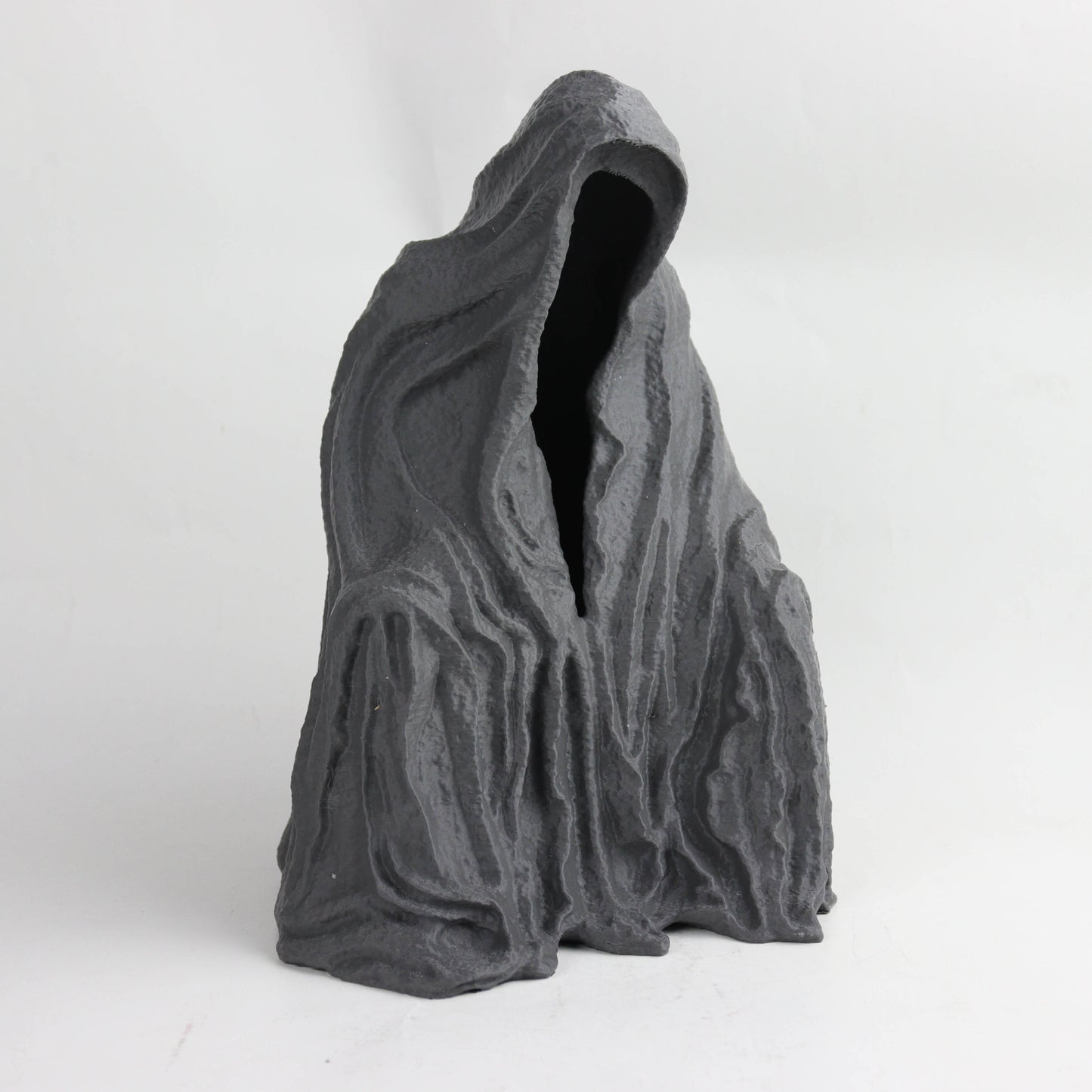A dark, abstract sculpture with a hooded figure and a textured, organic shape.