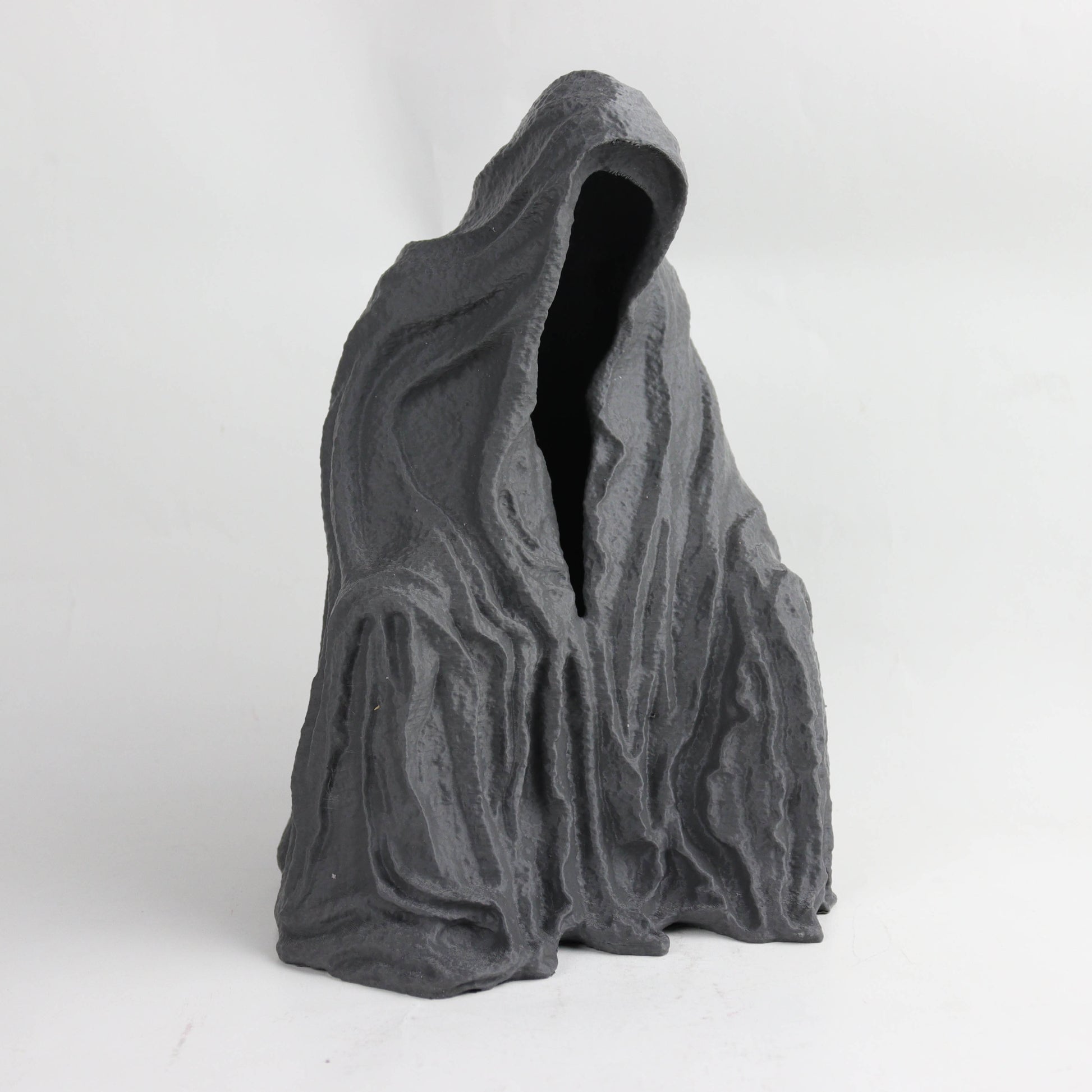 A dark, abstract sculpture with a hooded figure and a textured, organic shape.