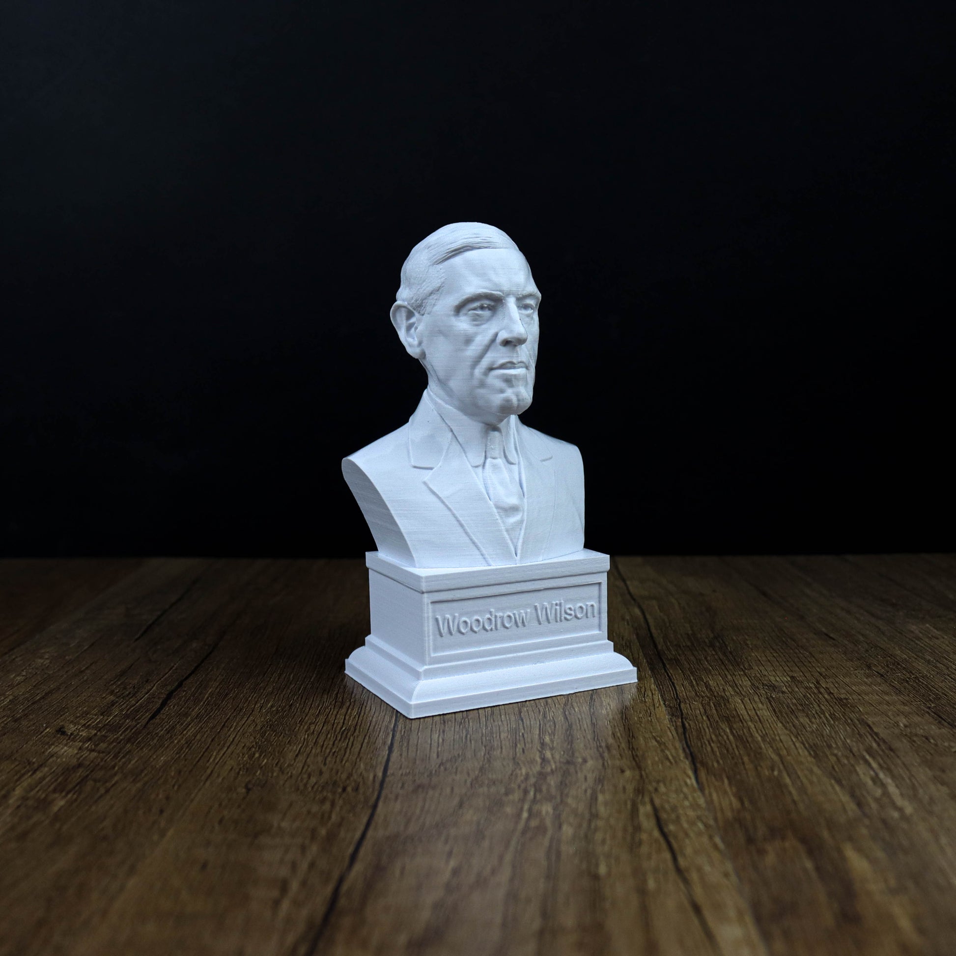 A white bust of a man is displayed on a wooden surface against a black background.