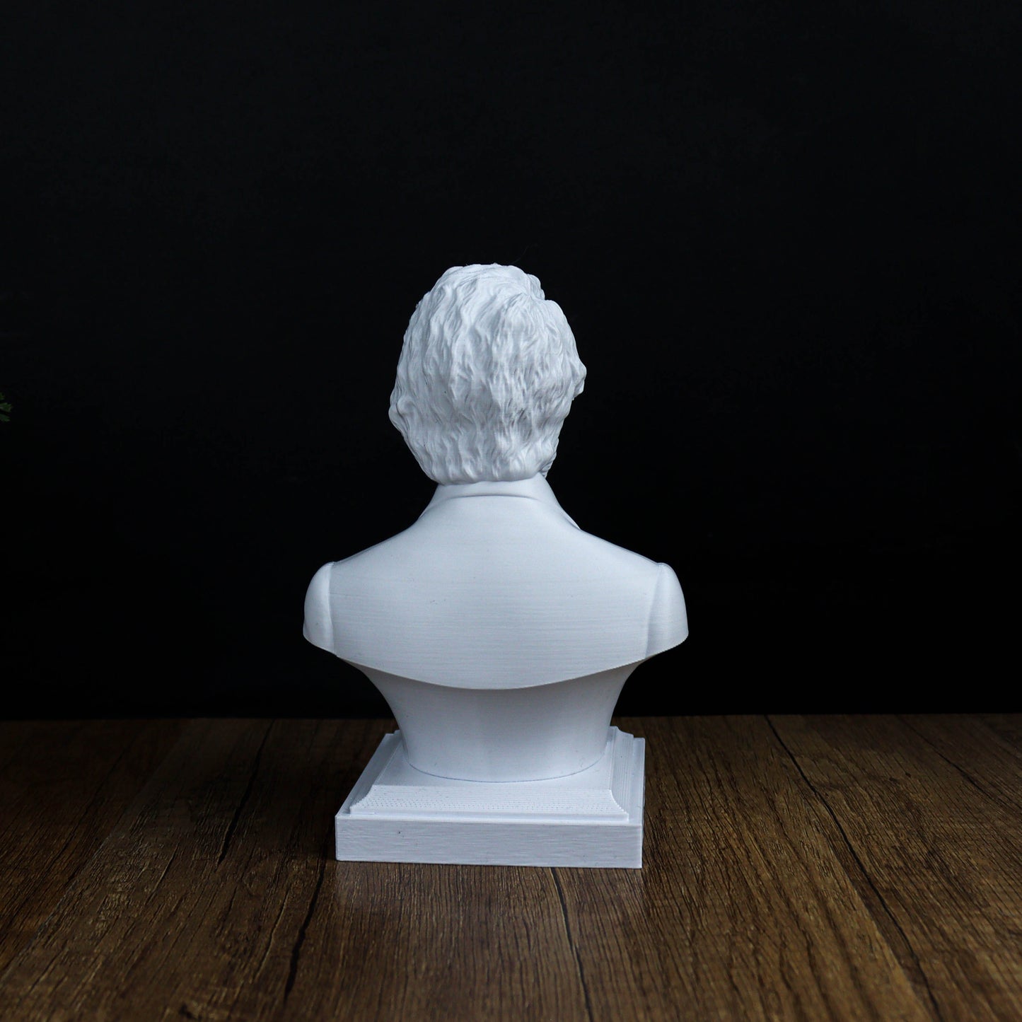 A white bust sculpture of a person is displayed on a wooden surface against a black background.